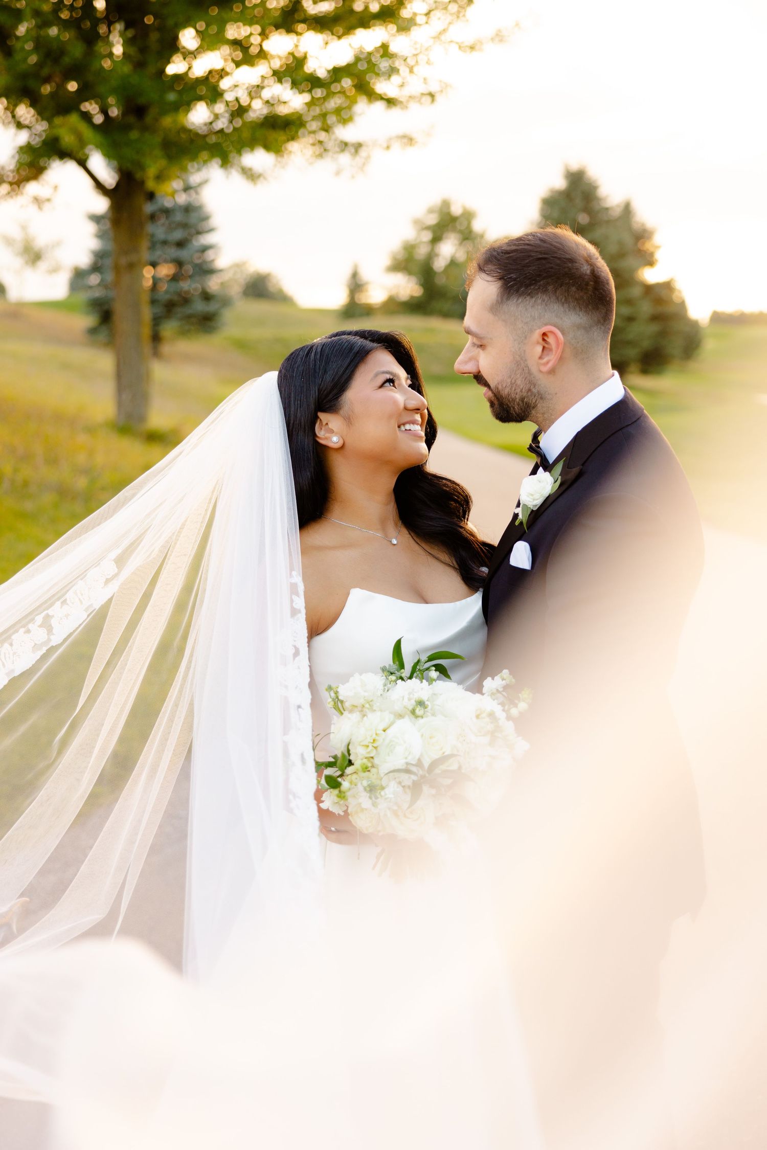 A candid wedding moment with the couple laughing together on a sun-lit golf course path.