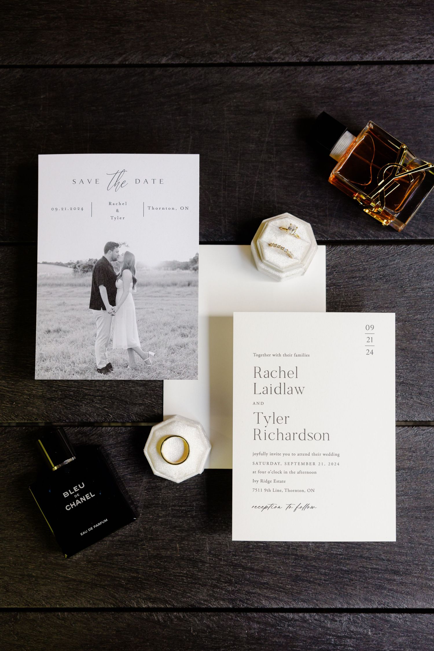 Wedding invitation suite with save the date card, perfume bottle, and ring box arranged on dark surface.