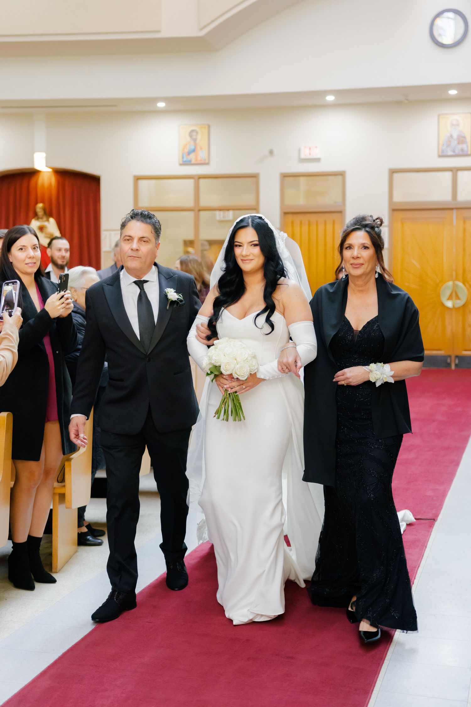 A wedding party processes down a red carpet aisle in a church setting.