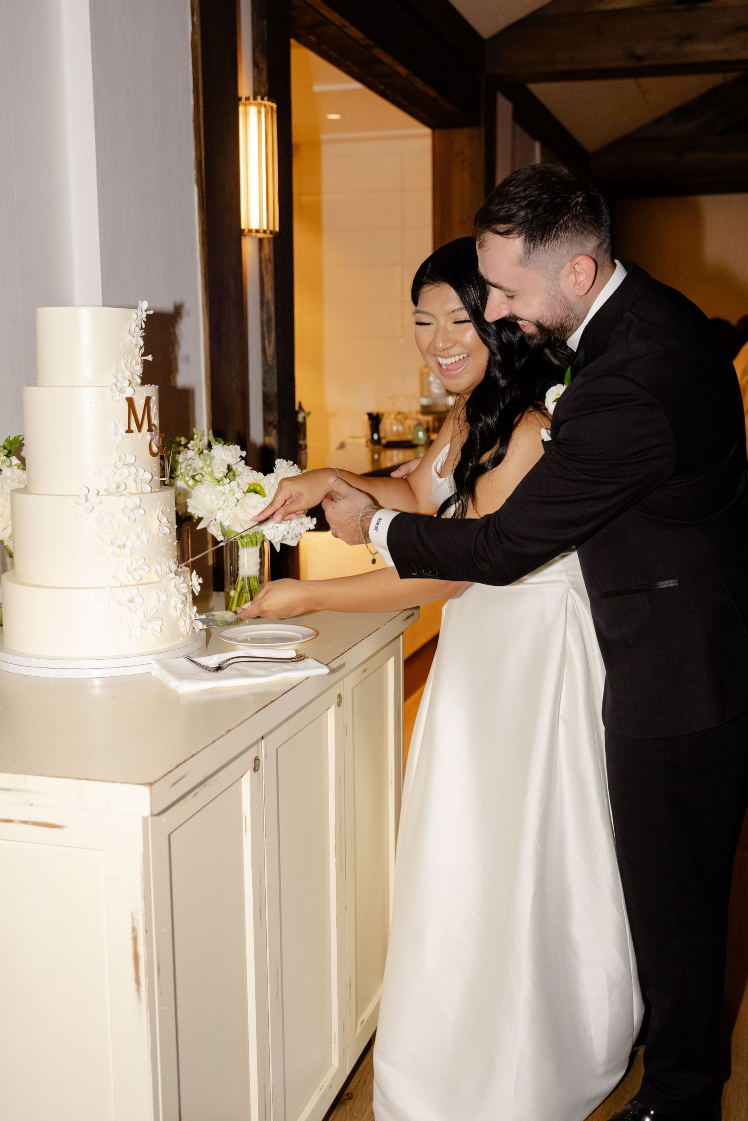 Wedding couple cuts their elegant white tiered cake together during reception.
