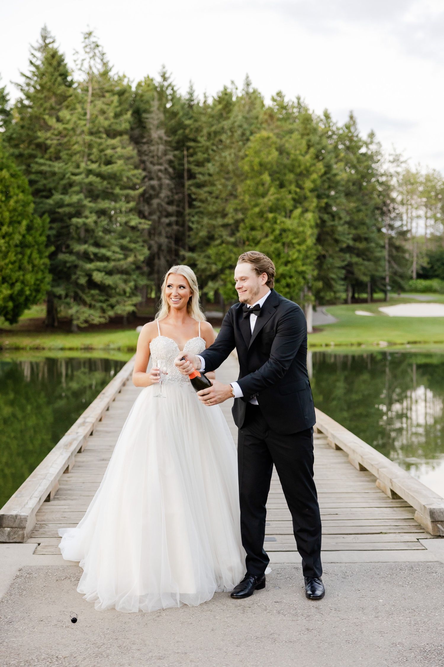 Joyful moment shared on wooden dock with evergreen forest and pond backdrop.