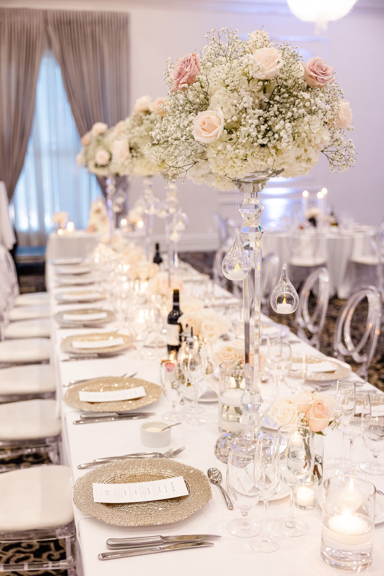 Elegant wedding reception table setting with tall floral centerpieces and crystal stemware on white linens.