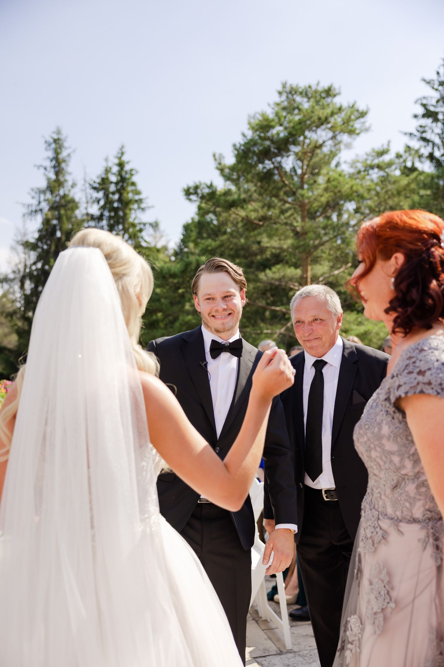 An intimate wedding ceremony moment captured on a sunny outdoor terrace with trees in background.