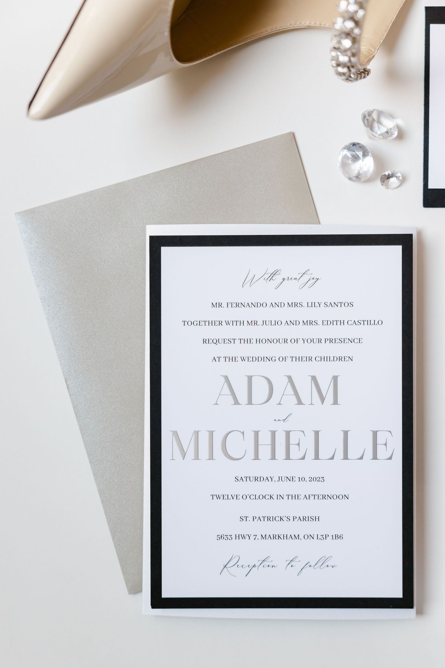 Modern black and white wedding invitation with silver accents and bridal accessories.
