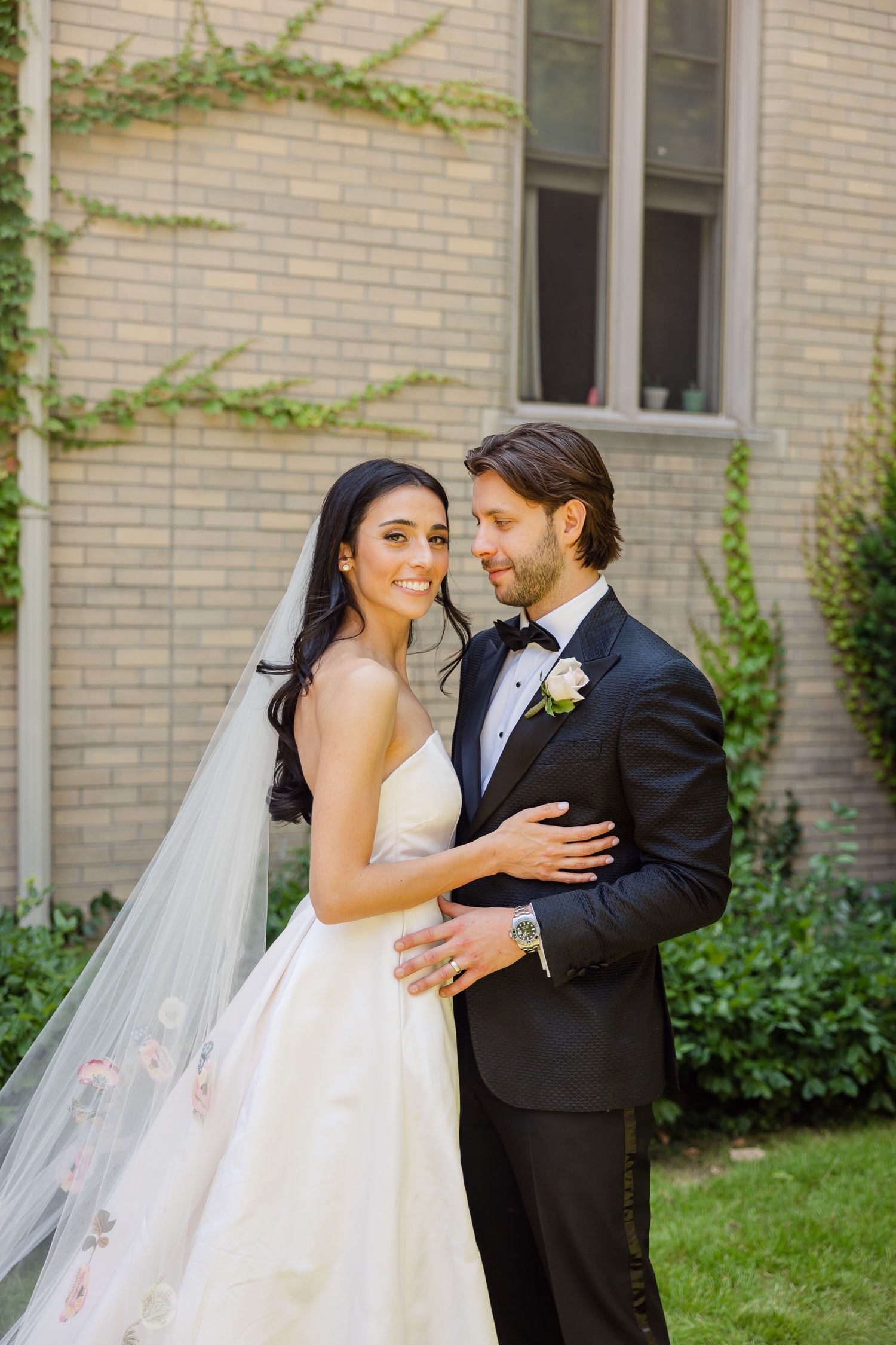 Elegant wedding portrait featuring a couple in formal attire against a classic brick building.
