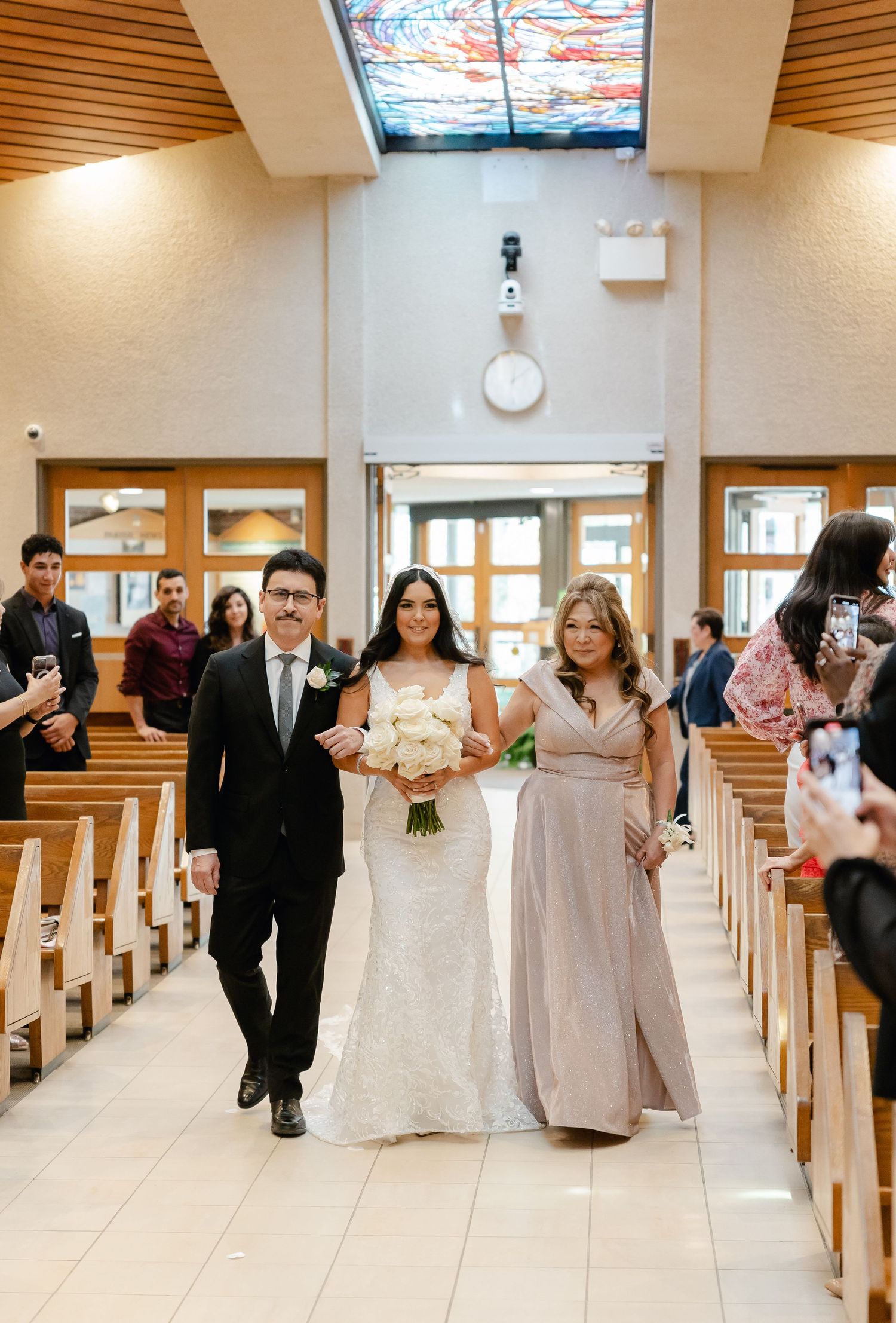Wedding party walks down church aisle with distinctive stained glass skylight overhead.