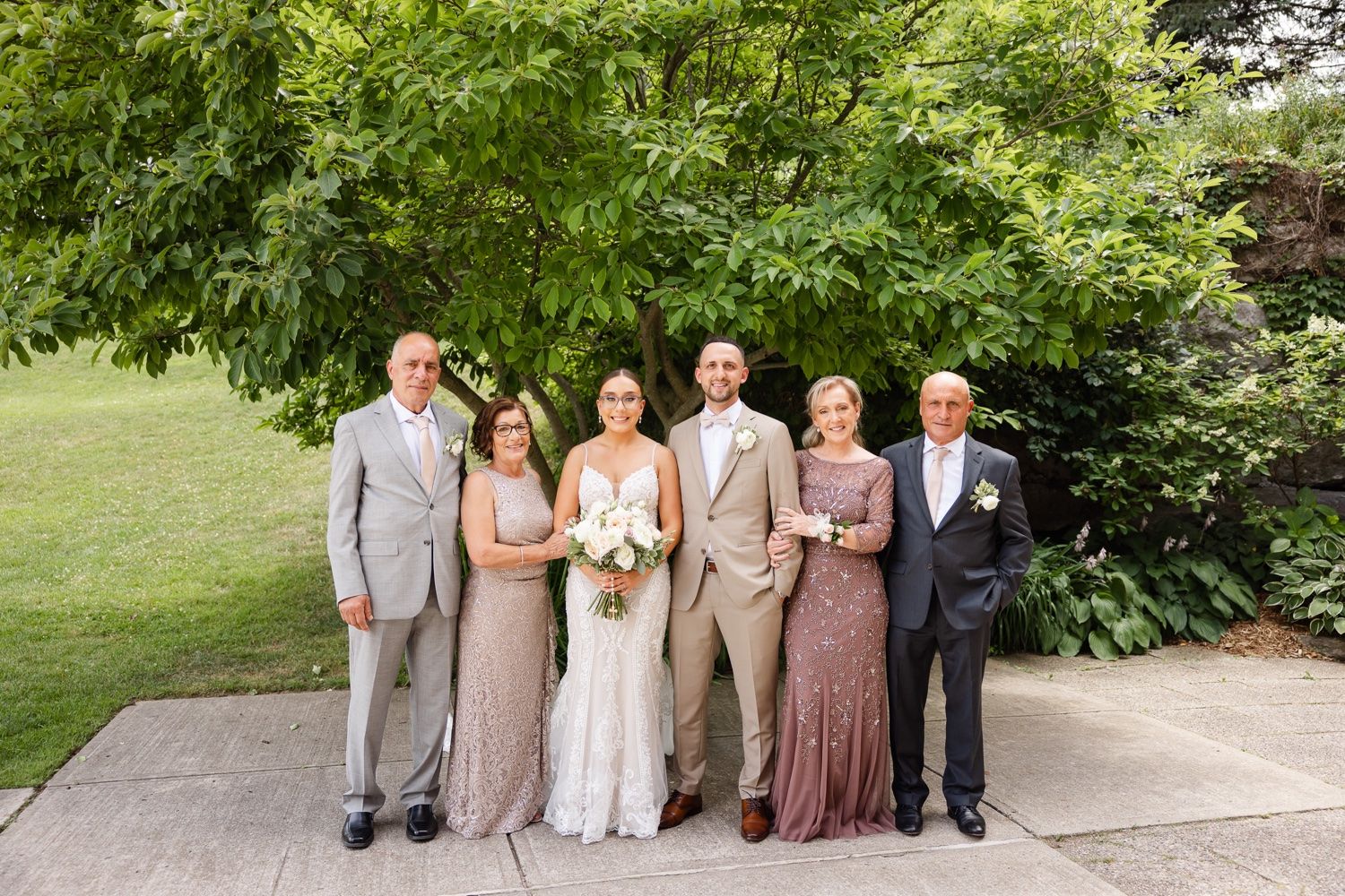 Formal wedding party group photo taken outdoors with coordinated neutral-colored attire.