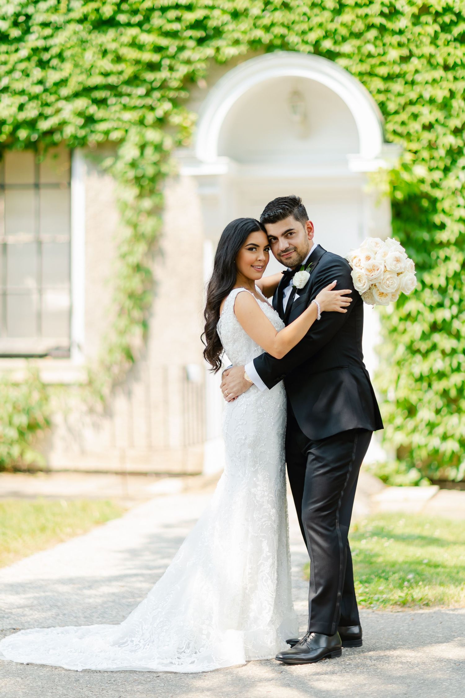 Romantic embrace between newlyweds in front of an ivy-covered building with white archway.