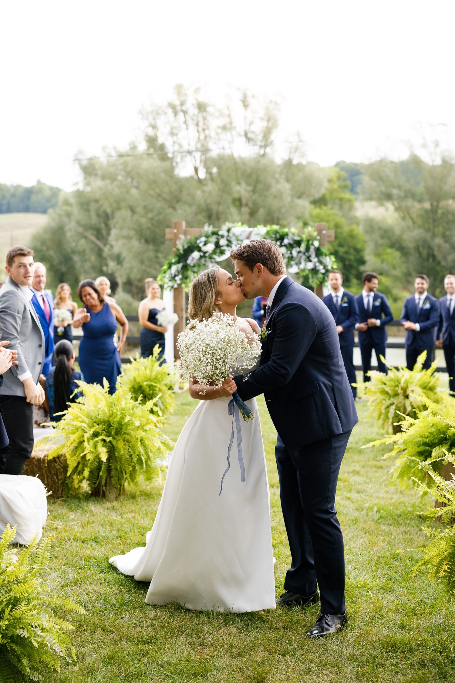 A romantic moment captured under a floral arch with yellow ferns decorating the outdoor ceremony space.