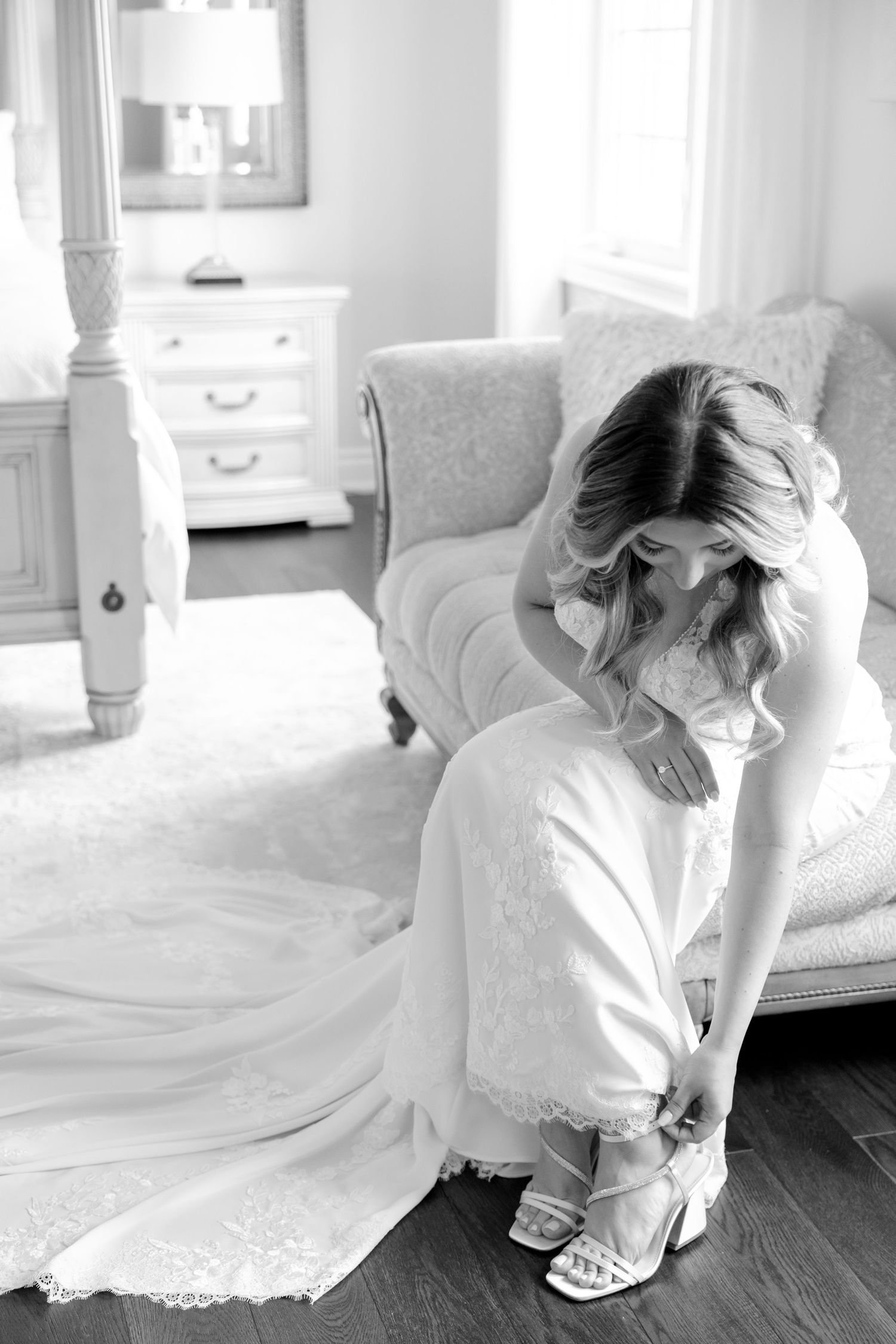 Black and white photo of getting ready moment adjusting wedding shoes on hardwood floor.