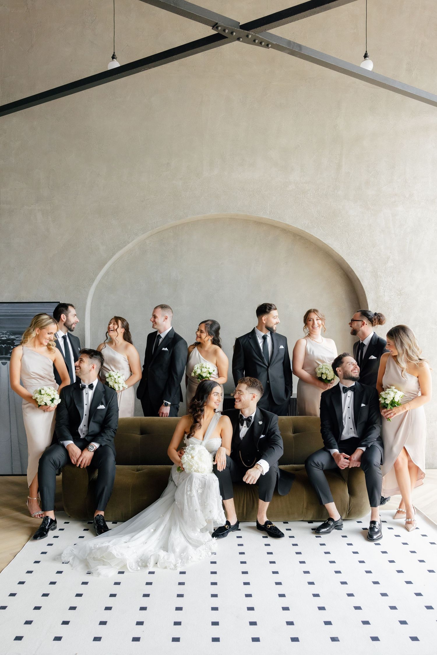 Wedding party arranged around a tan couch with bridesmaids in blush and groomsmen in black.