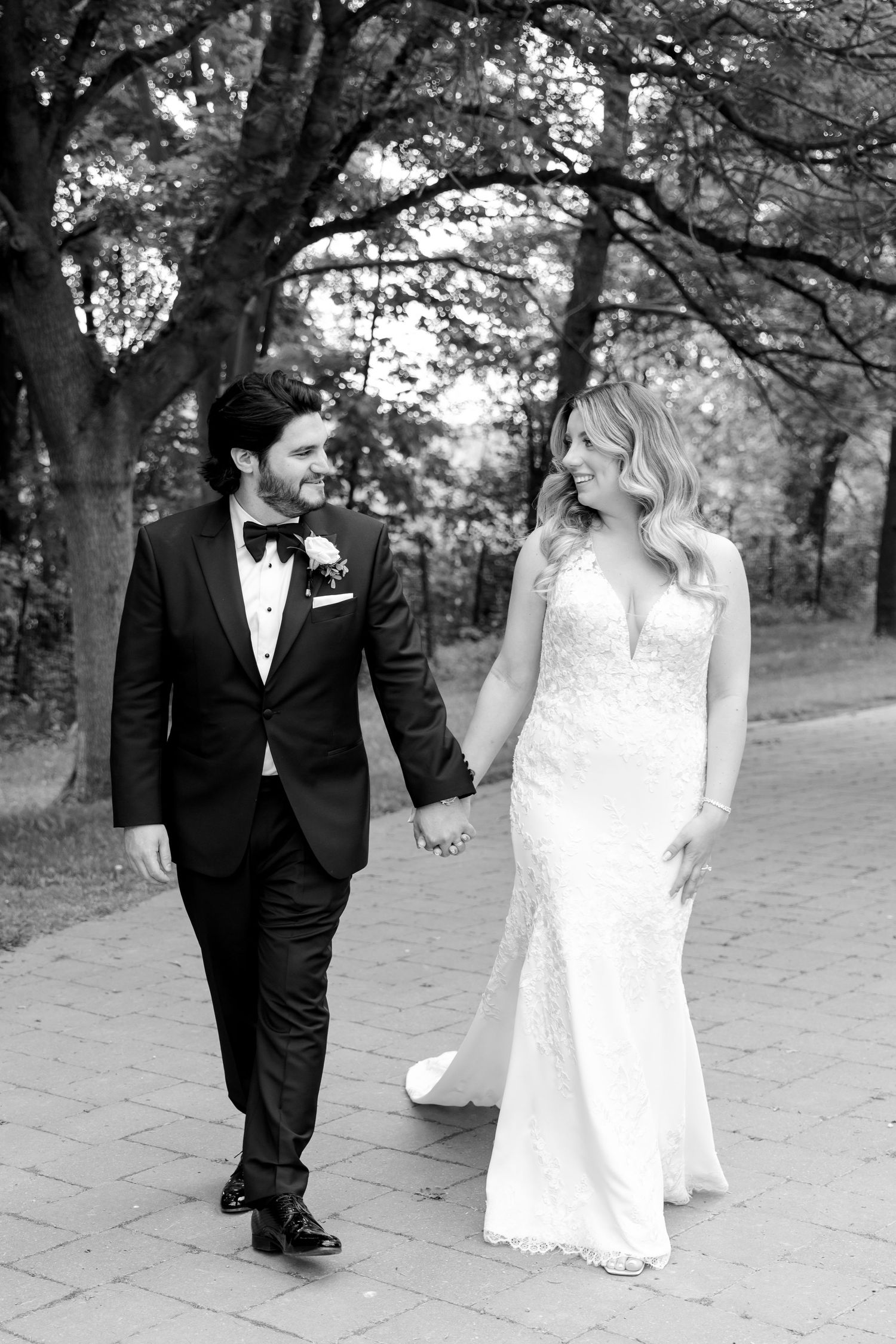 Black and white photo of newlyweds walking together on a garden path.