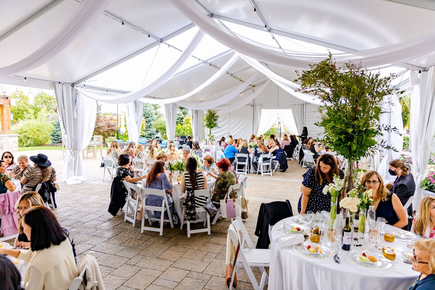 Wedding reception setup under white tent with round tables and elegant decor.