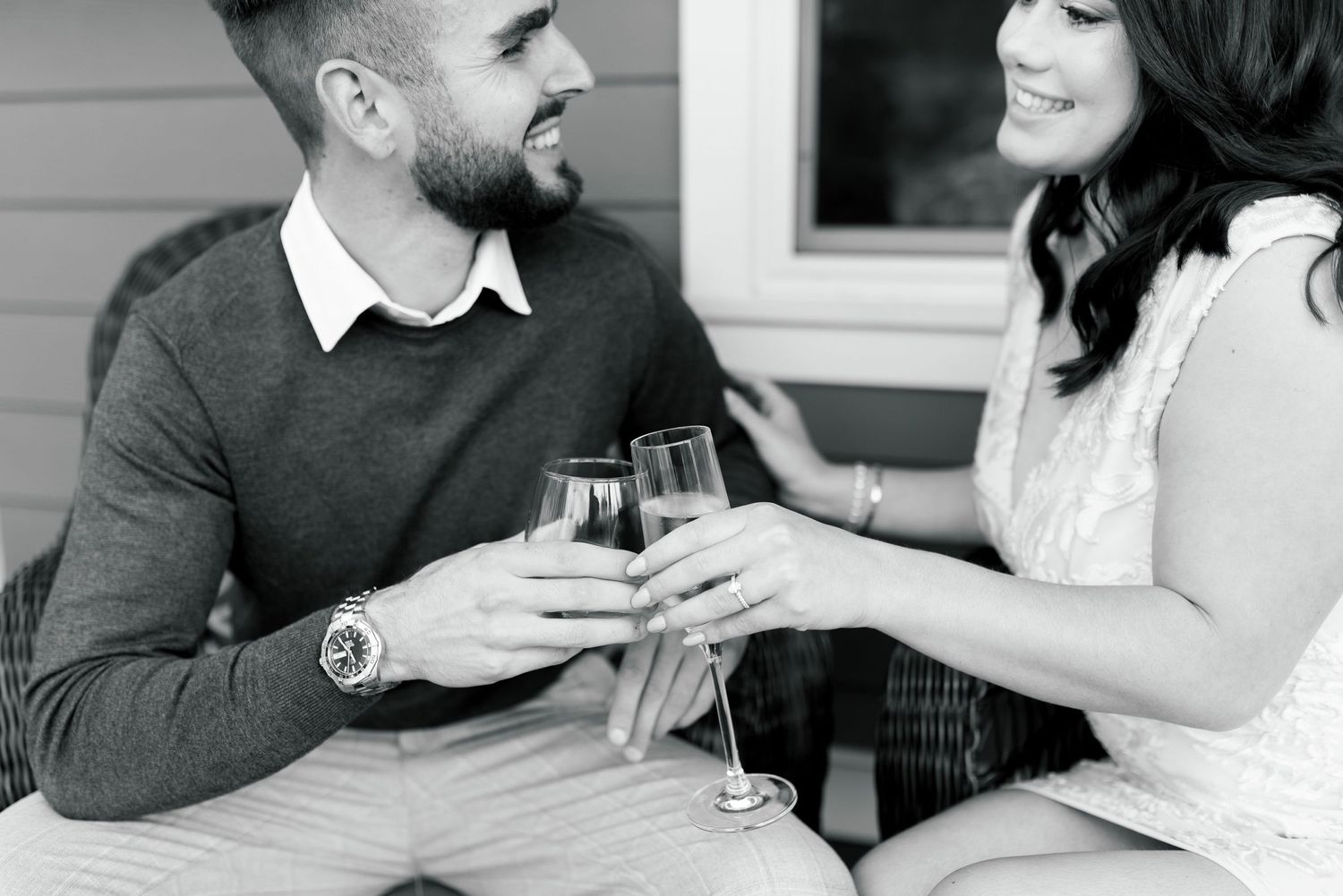 A black and white image of two people toasting with wine glasses on a porch.