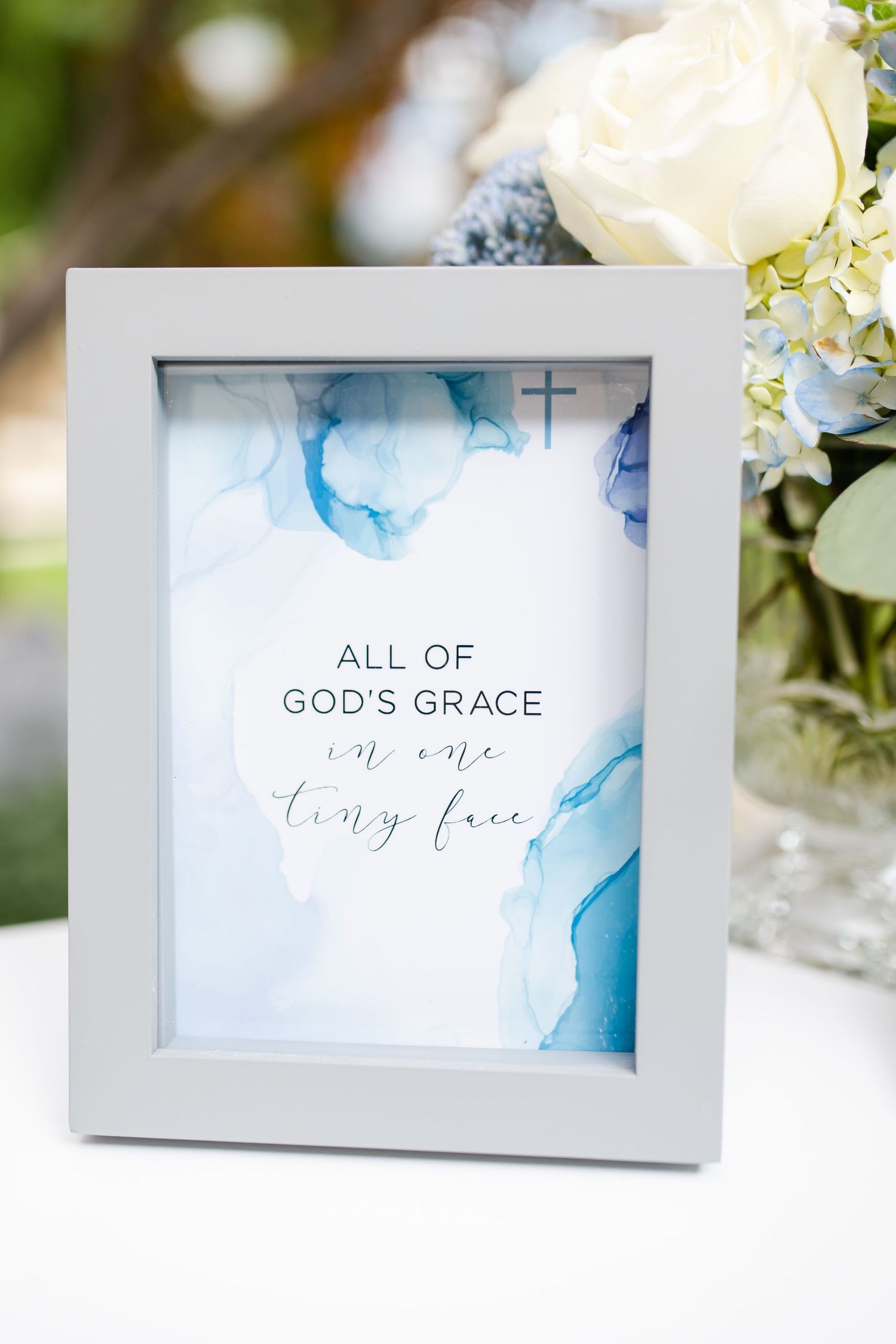 A framed sign reading 'All of God's Grace' with blue watercolor design and white flowers.