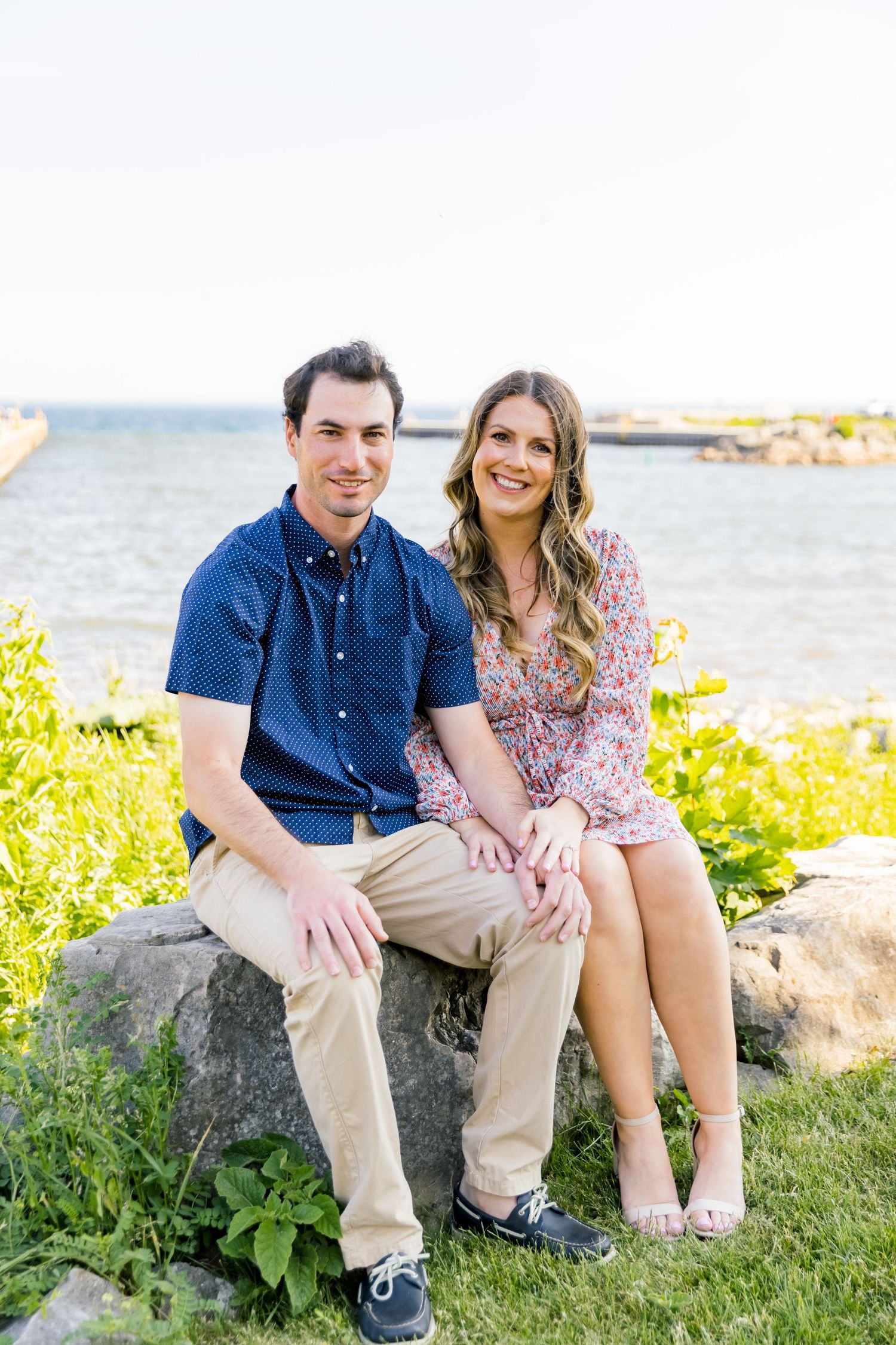 A couple in summer attire sitting together on coastal rocks with ocean view.