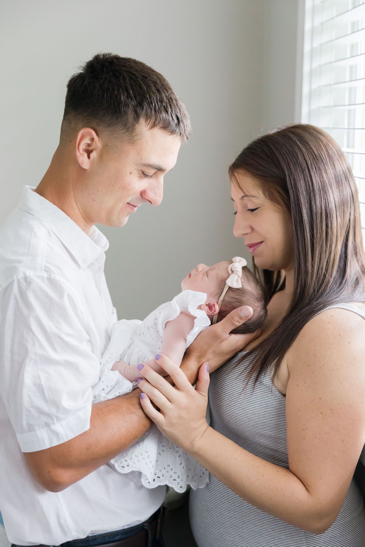 Intimate portrait of parents bonding with their newborn baby in white lace dress.