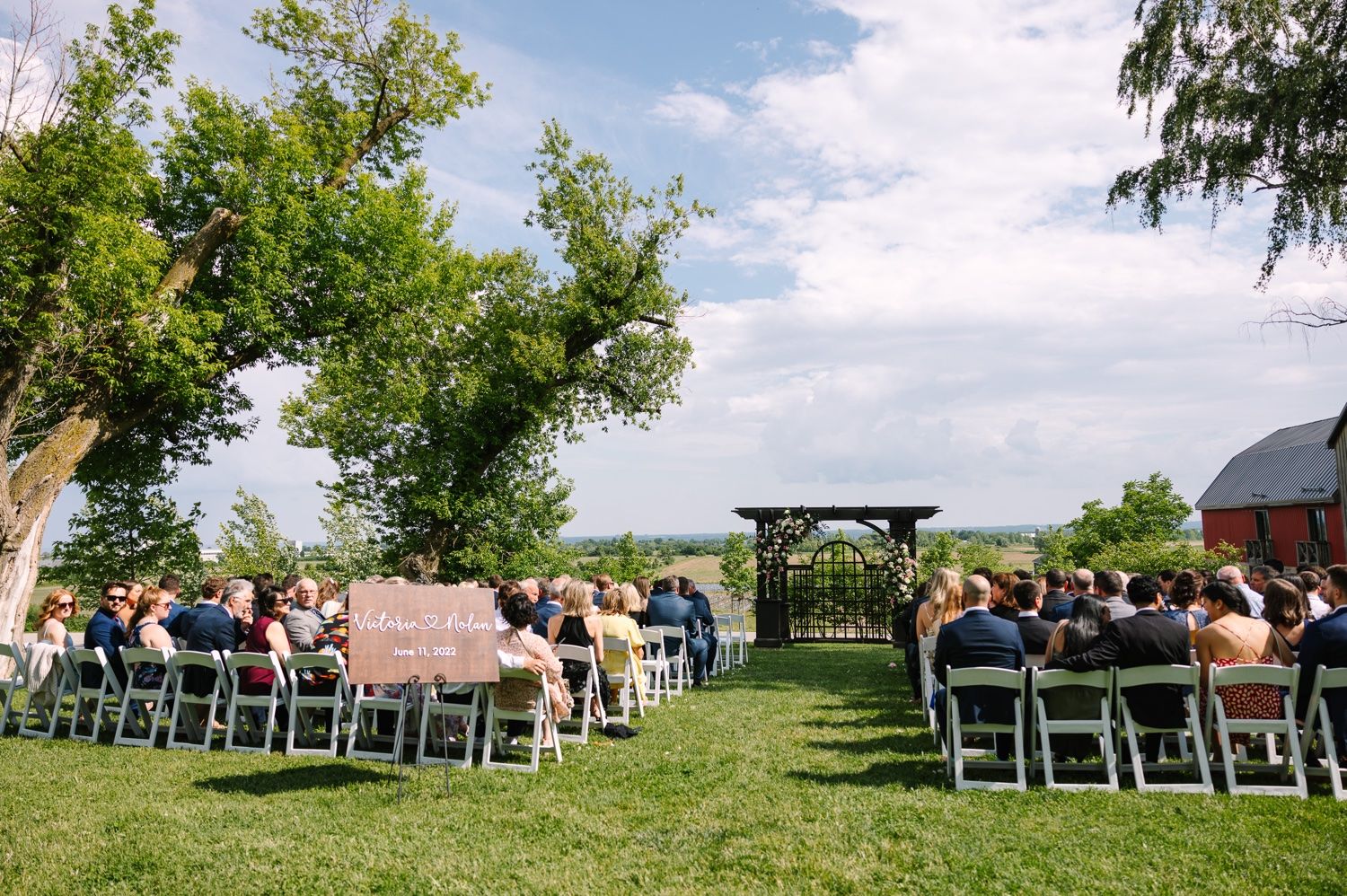 Outdoor wedding ceremony setup with white chairs and wooden arch on green lawn.