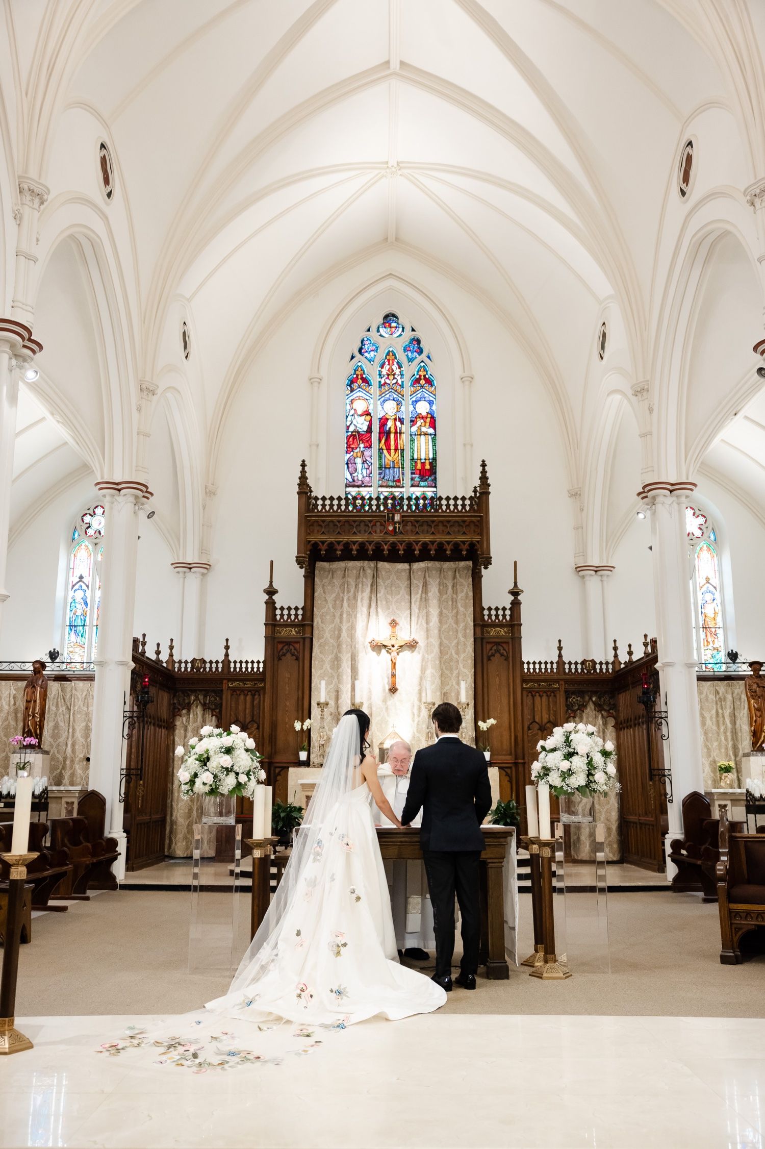 An elegant church interior with vaulted ceilings, stained glass windows, and wooden altar during a wedding ceremony.
