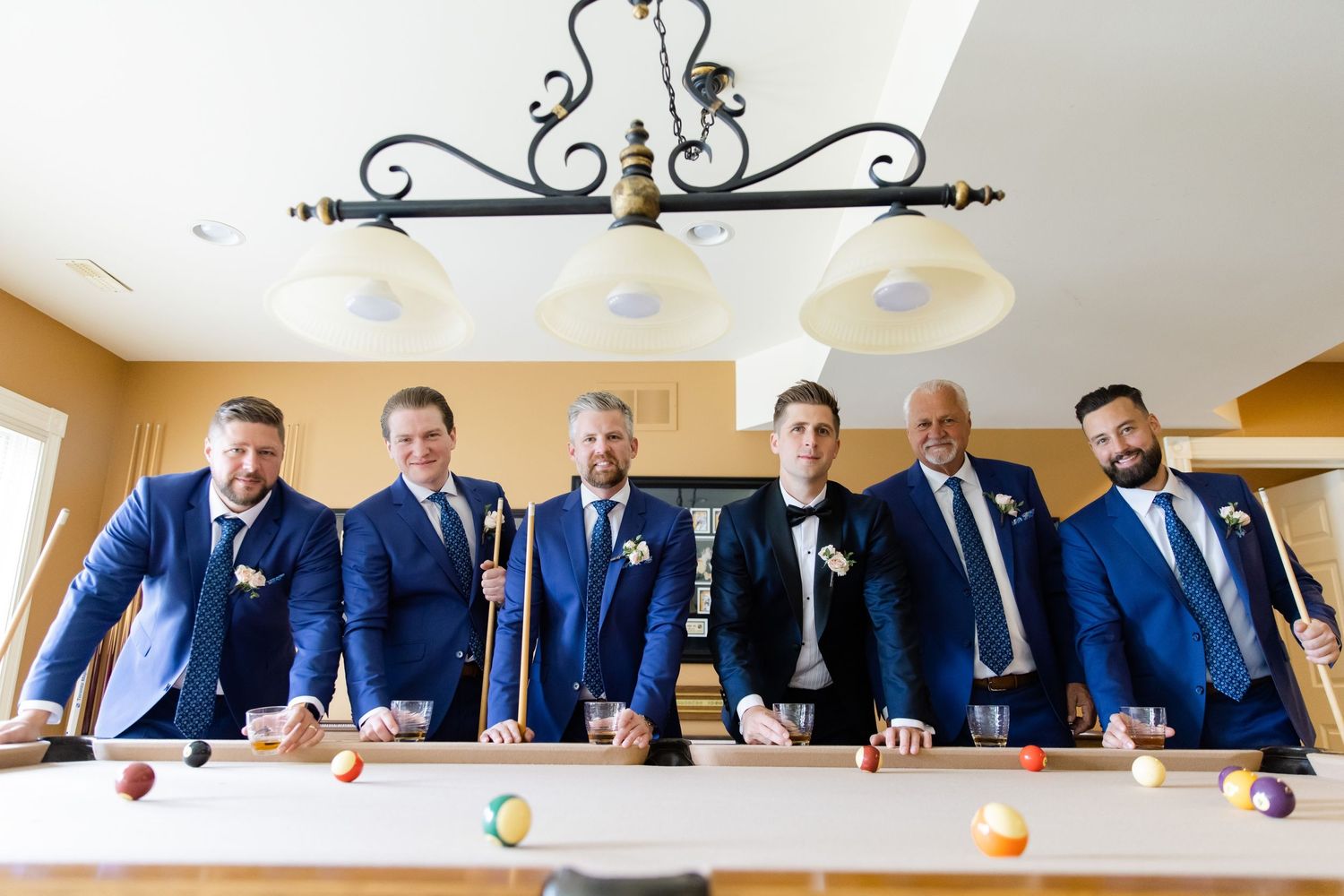 Groomsmen in navy suits pose together at a pool table.