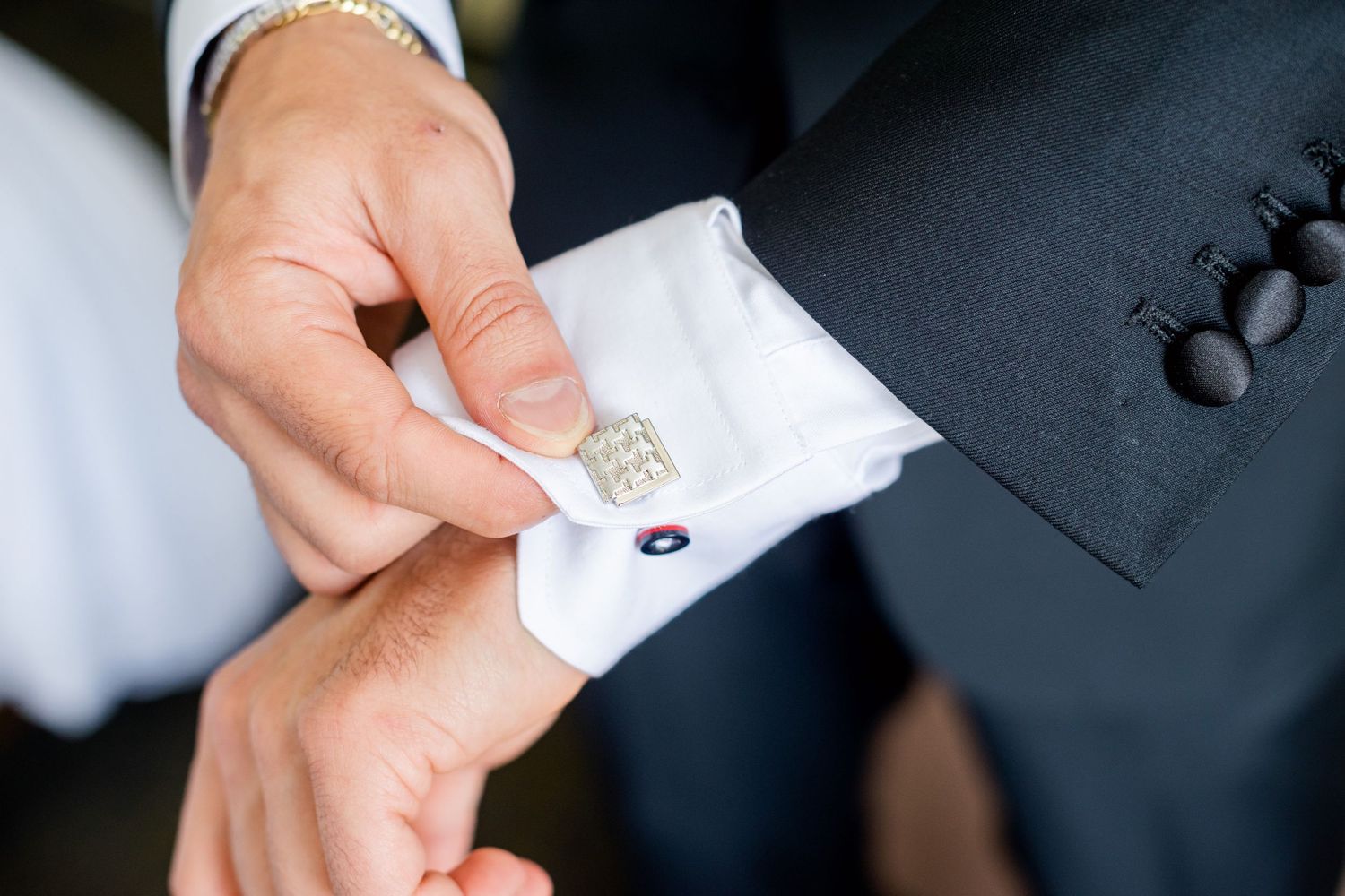 Close-up of hands adjusting a decorative cufflink on a formal white dress shirt sleeve.