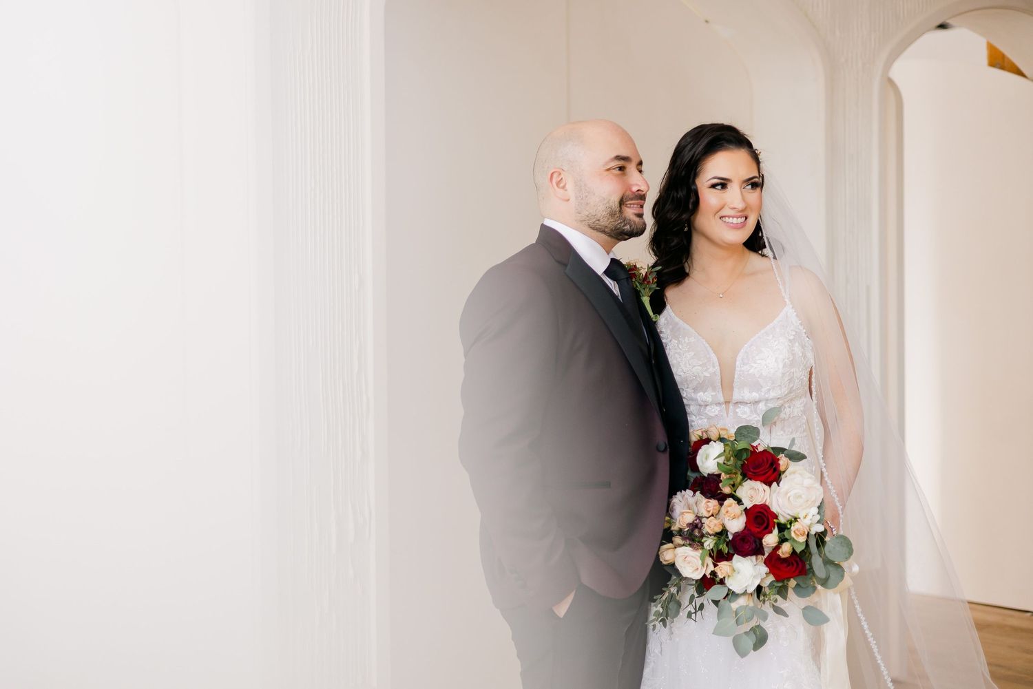 Intimate wedding portrait with couple standing close together against white wall.