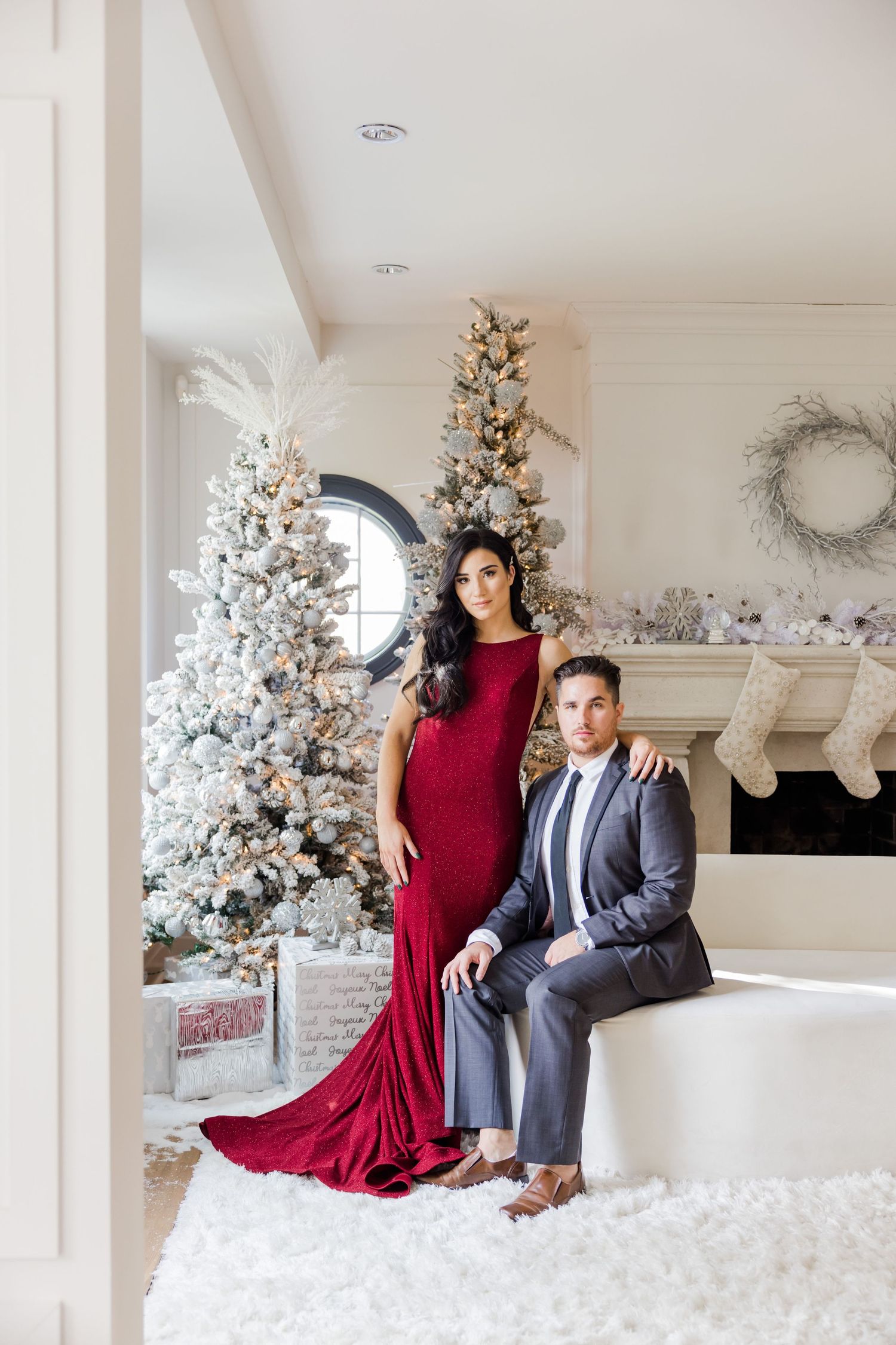 Formal portrait featuring red velvet gown and gray suit against snowy Christmas decor.