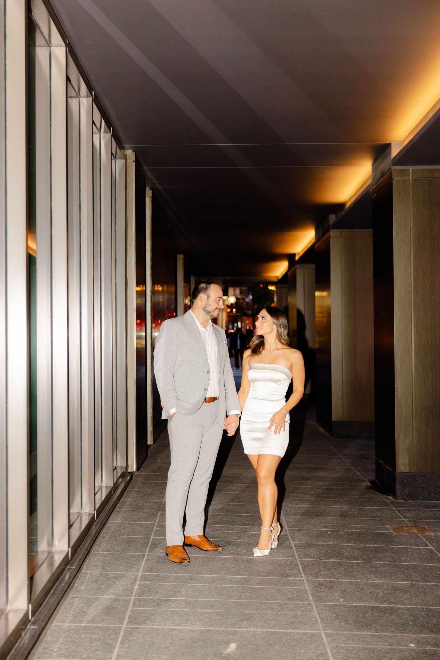 Couple sharing a romantic moment in a modern hallway with dramatic lighting.