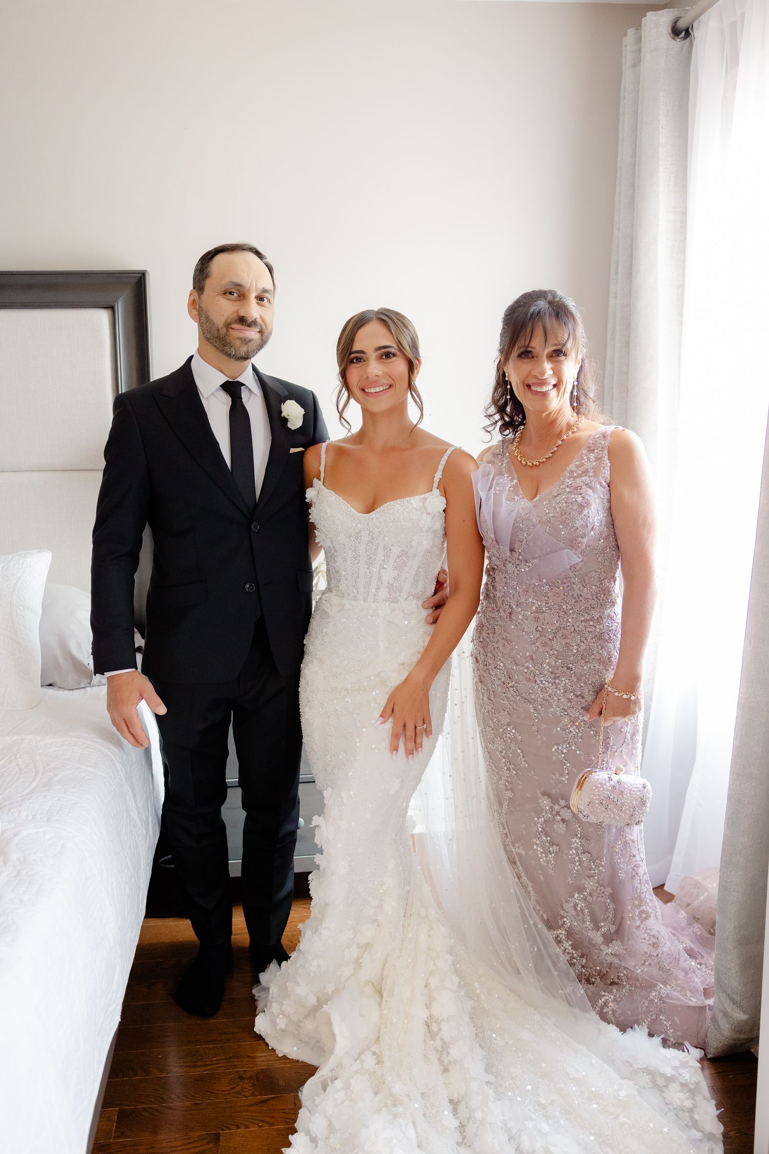 Three people in formal attire standing together at a wedding, with the bride wearing a beautiful white lace gown.
