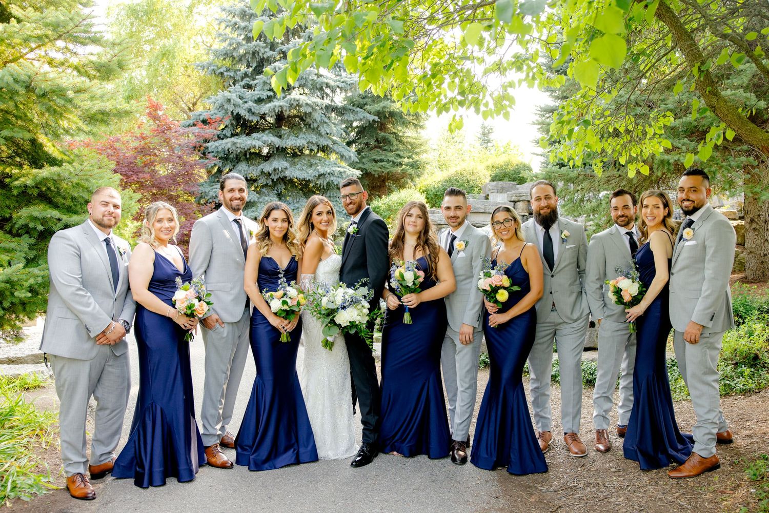 Full wedding party portrait with bridesmaids in navy gowns and groomsmen in light gray suits.