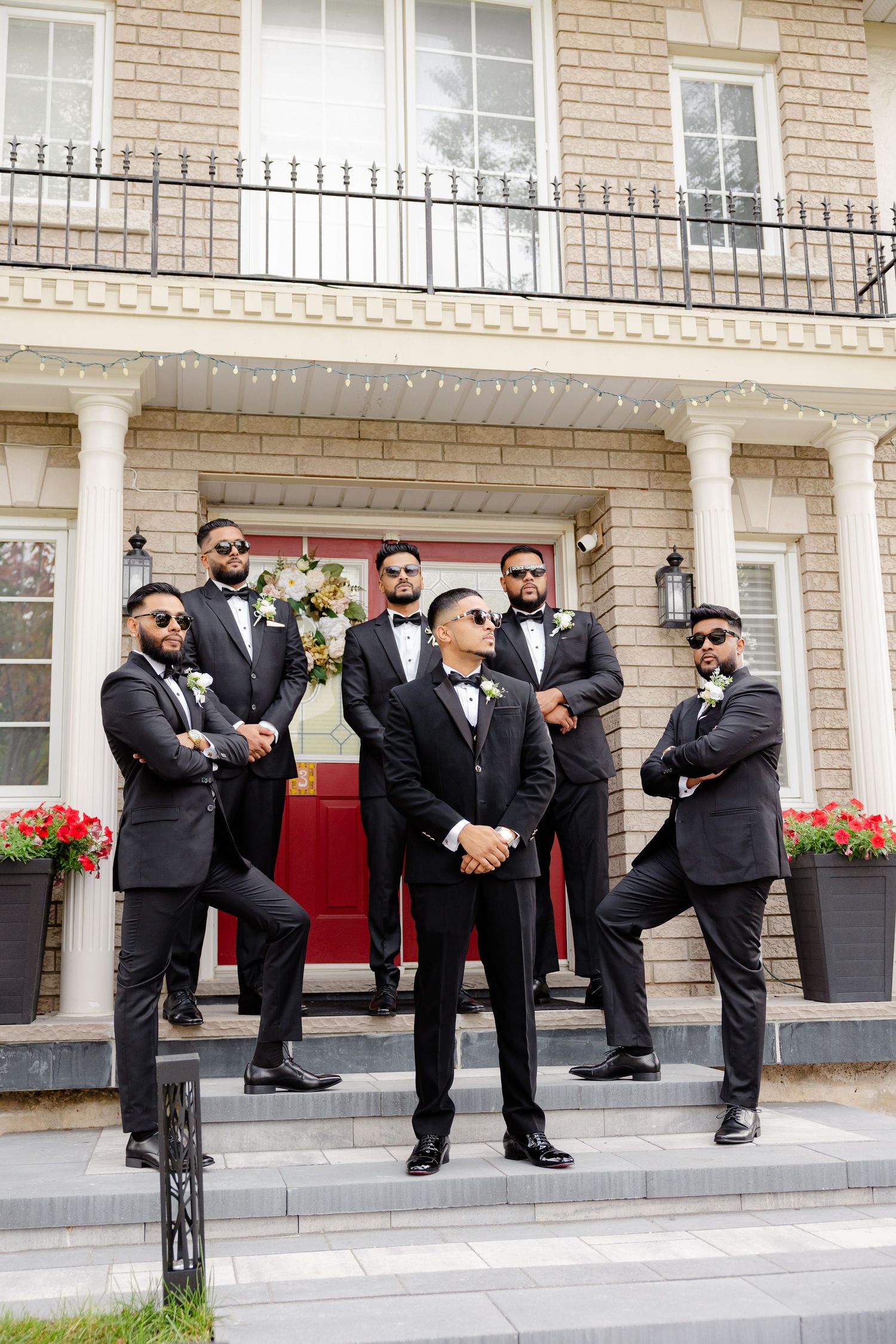 Stylish groomsmen strike casual poses on elegant stone steps of mansion.