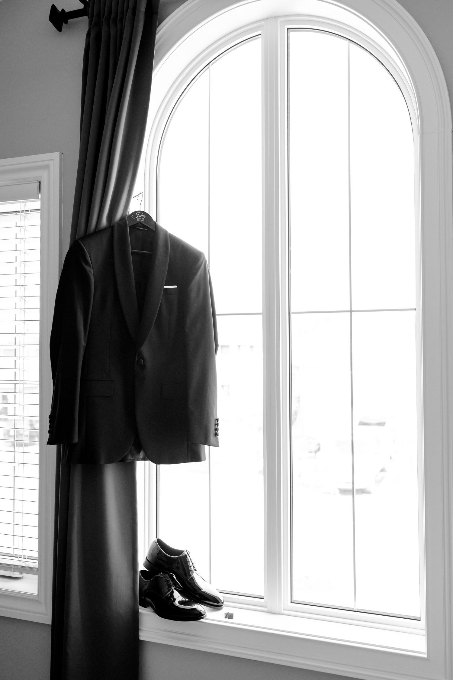 A black suit jacket and dress shoes artfully displayed in front of an arched window.