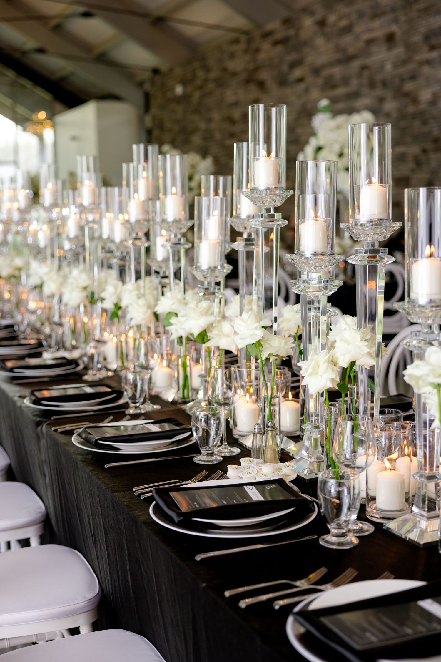 Long banquet table with crystal candle holders and white flowers on black tablecloth.