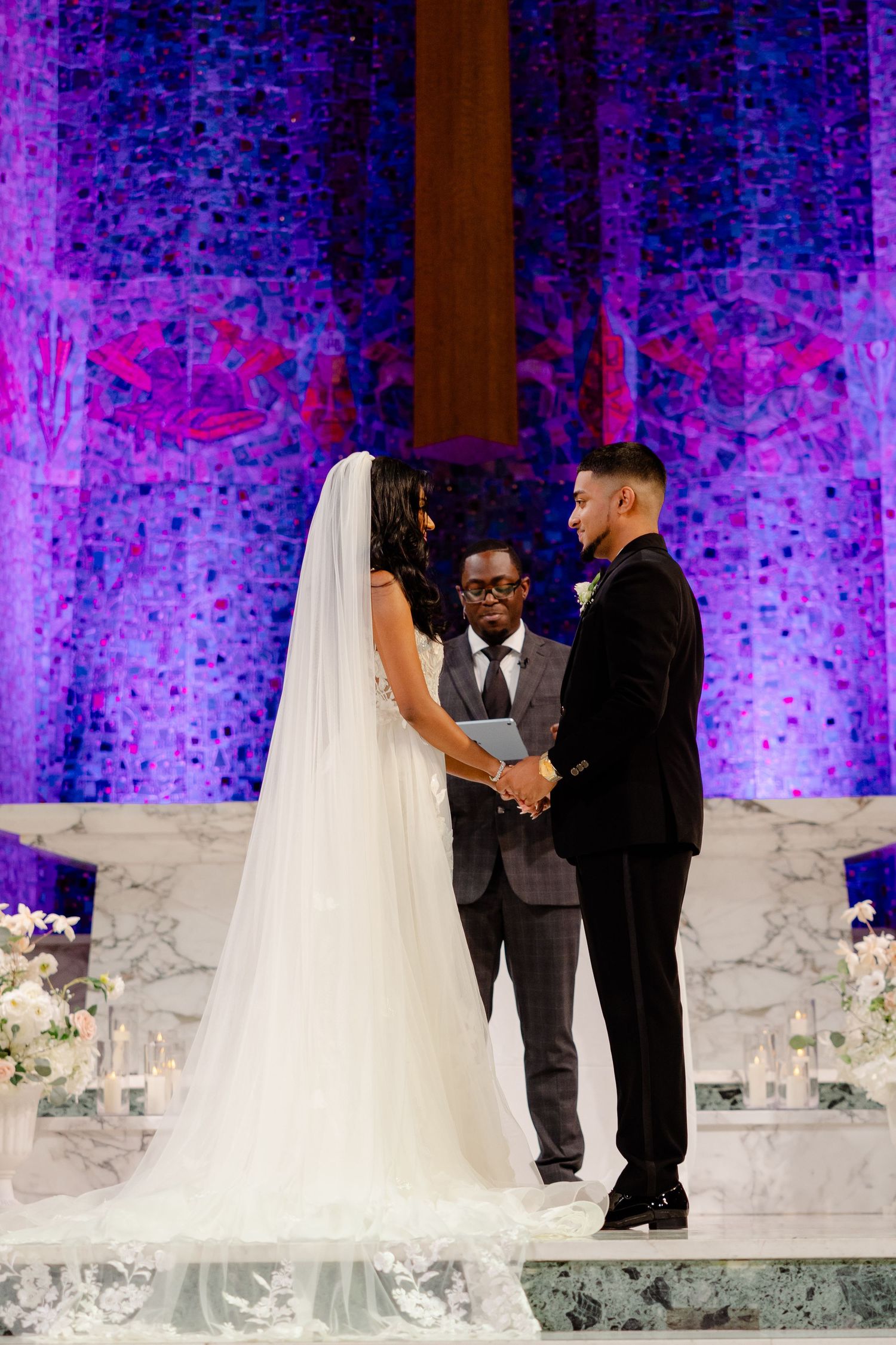 Wedding ceremony beneath purple-lit church backdrop with stunning architectural details.