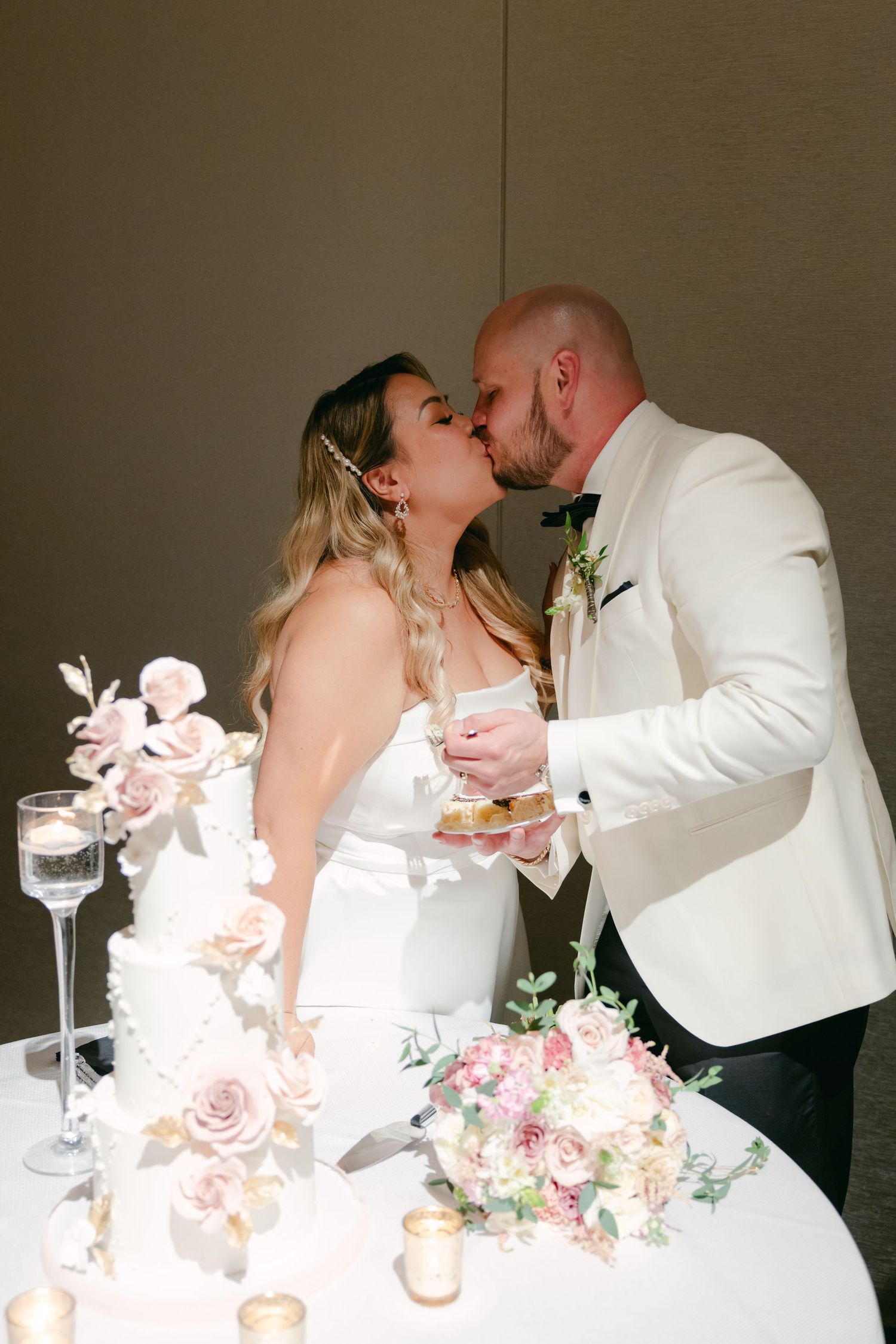 Romantic cake cutting moment at a wedding reception with pink floral decorations and champagne glasses.