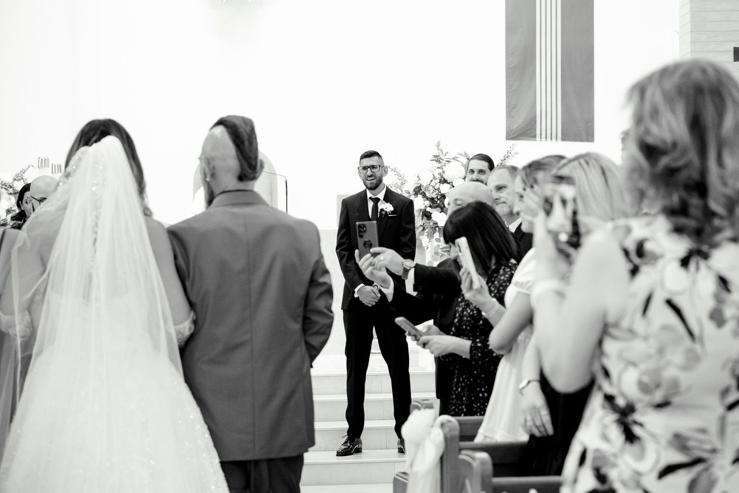 A black and white photo capturing a wedding ceremony moment in a modern church setting.