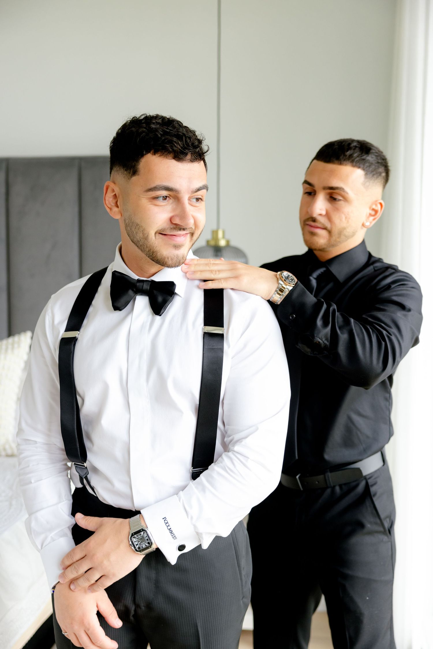 Elegant formal wear featuring crisp white shirt, bow tie and black suspenders in bright room.