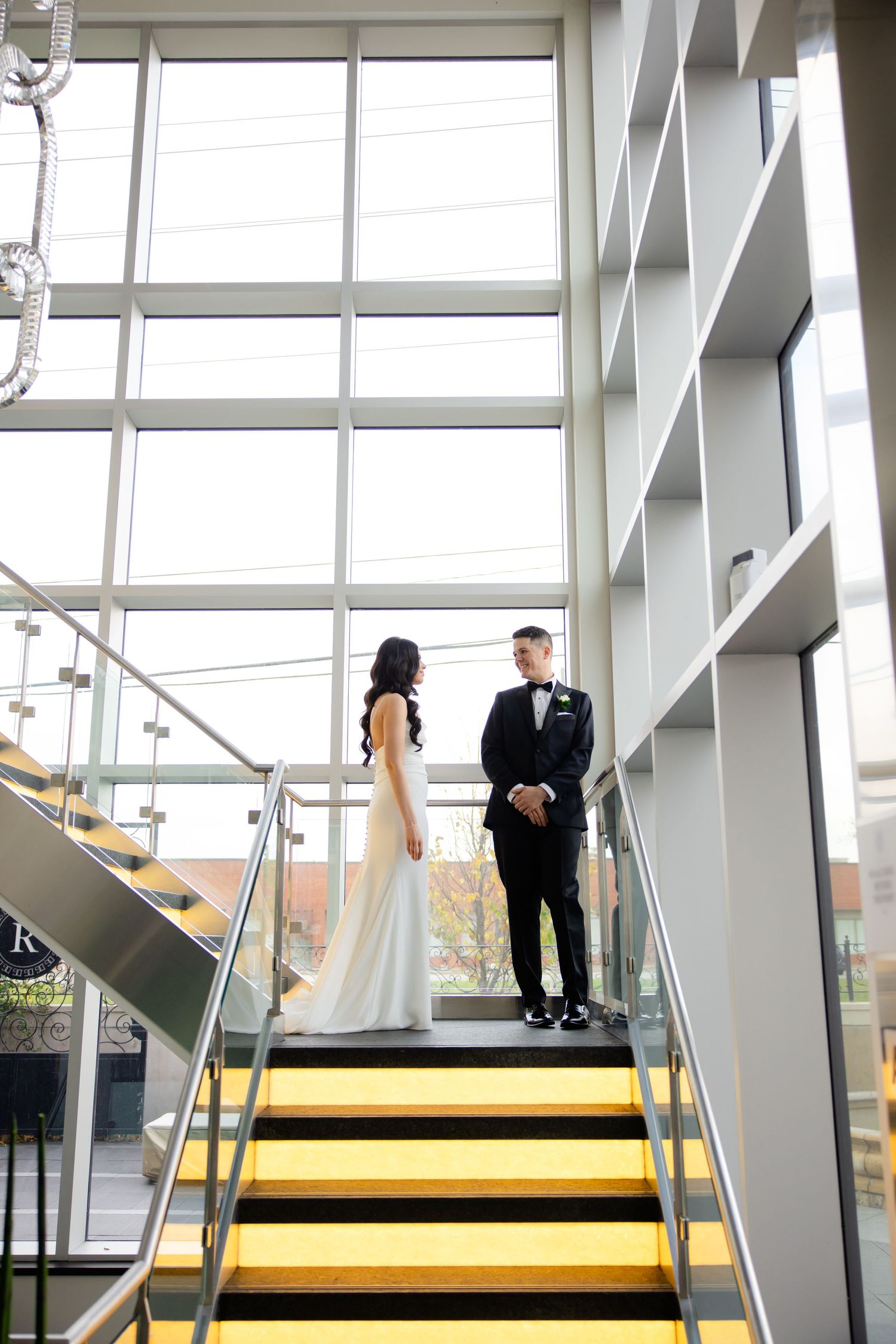 Wedding portrait on modern yellow and black staircase framed by floor-to-ceiling windows.