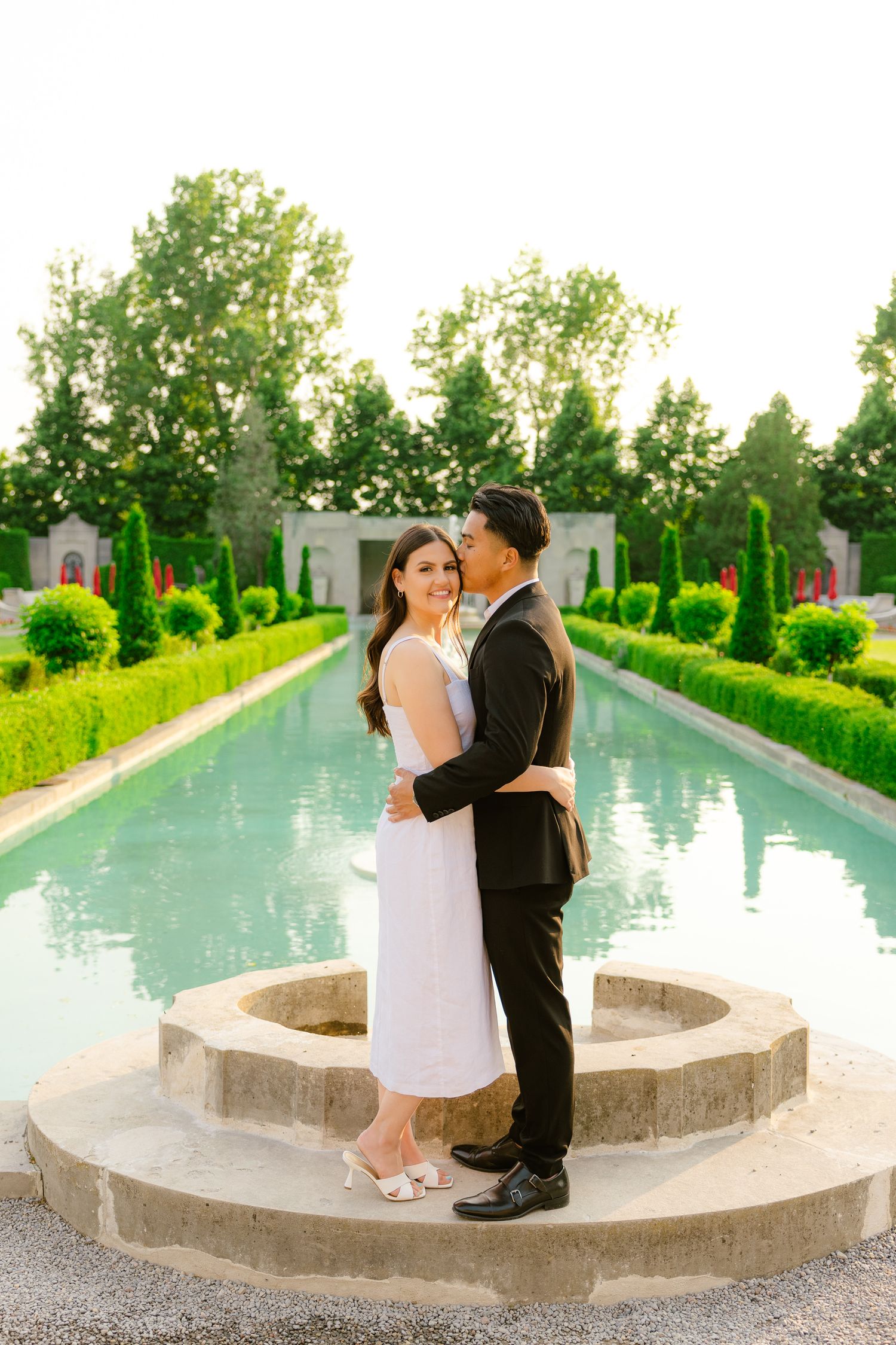 A couple in formal attire sharing a romantic moment by a garden fountain.