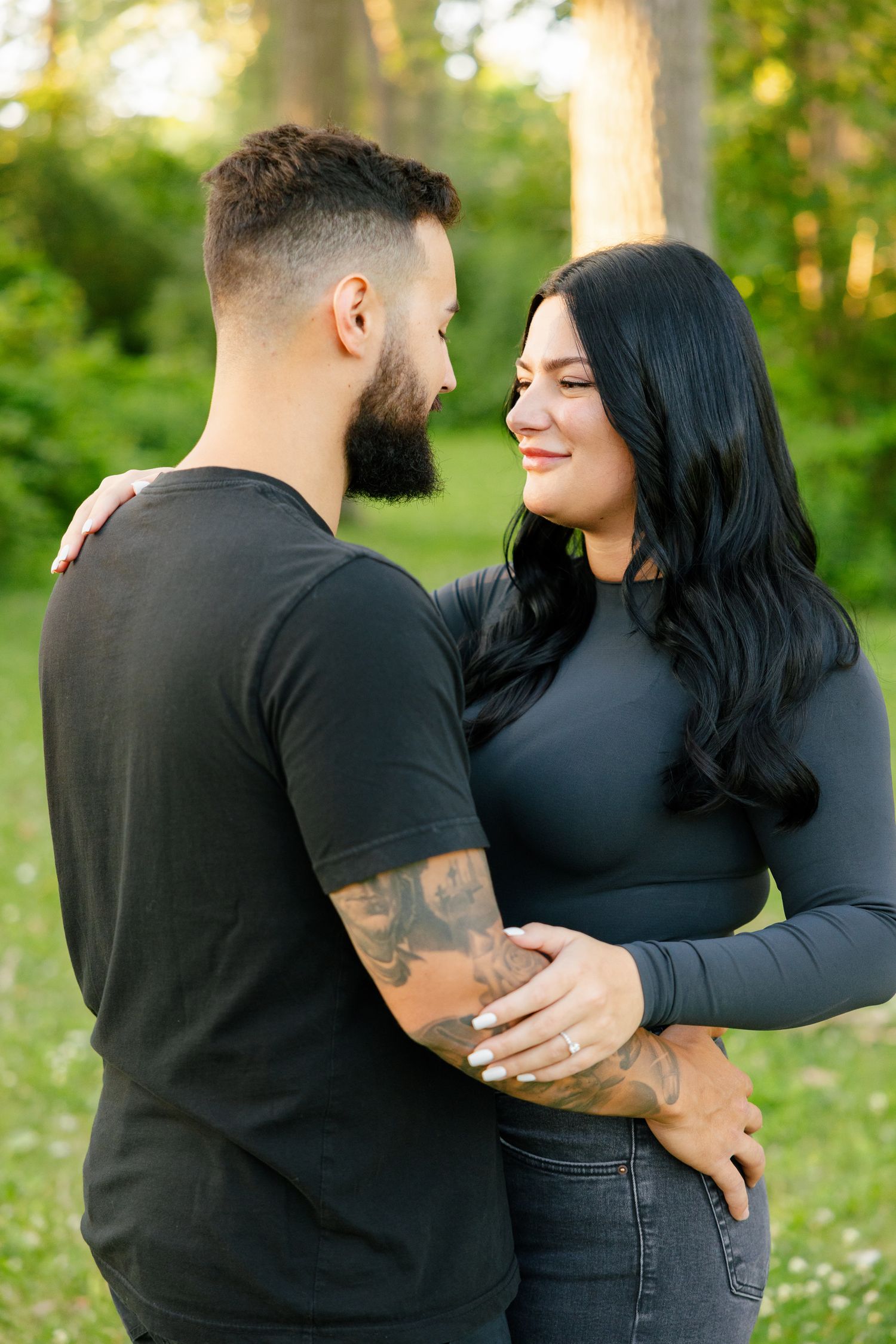 Close-up of couple in black clothing sharing an intimate moment in a sunny forest clearing.