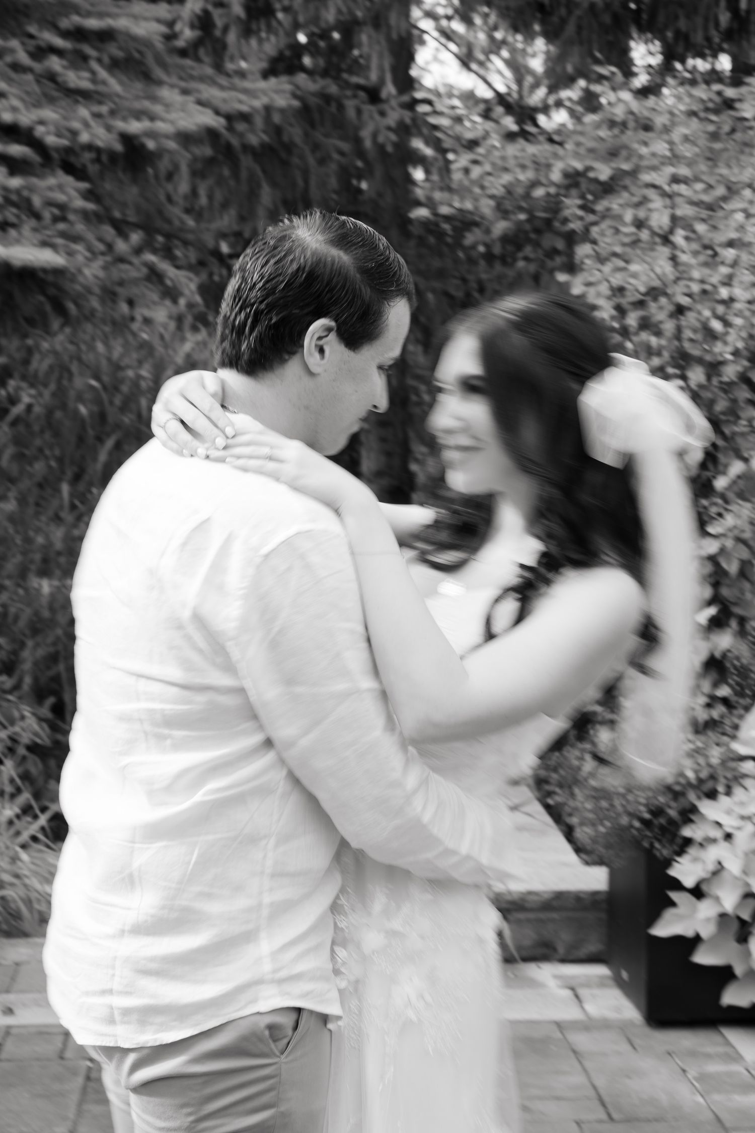 A black and white photo captures a joyful spinning dance moment between newlyweds in a garden.