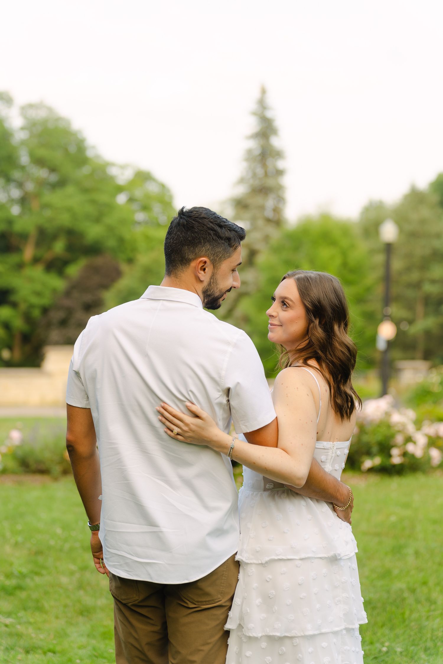A tender moment between a couple standing in a beautiful garden setting with evergreen trees.