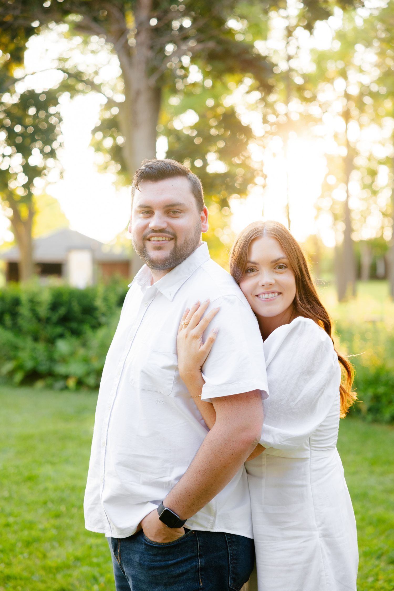 Joyful couple in white clothing pose together in a backyard garden during sunset.