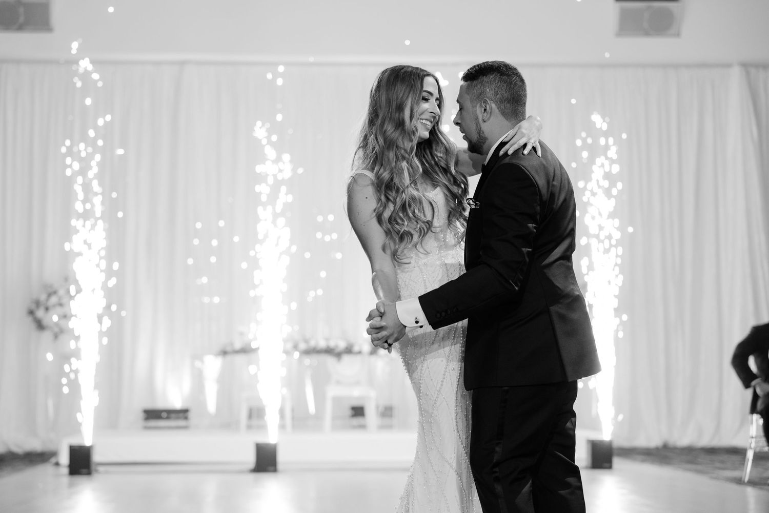 Black and white photo of romantic dance with sparkler effects in elegant reception hall.