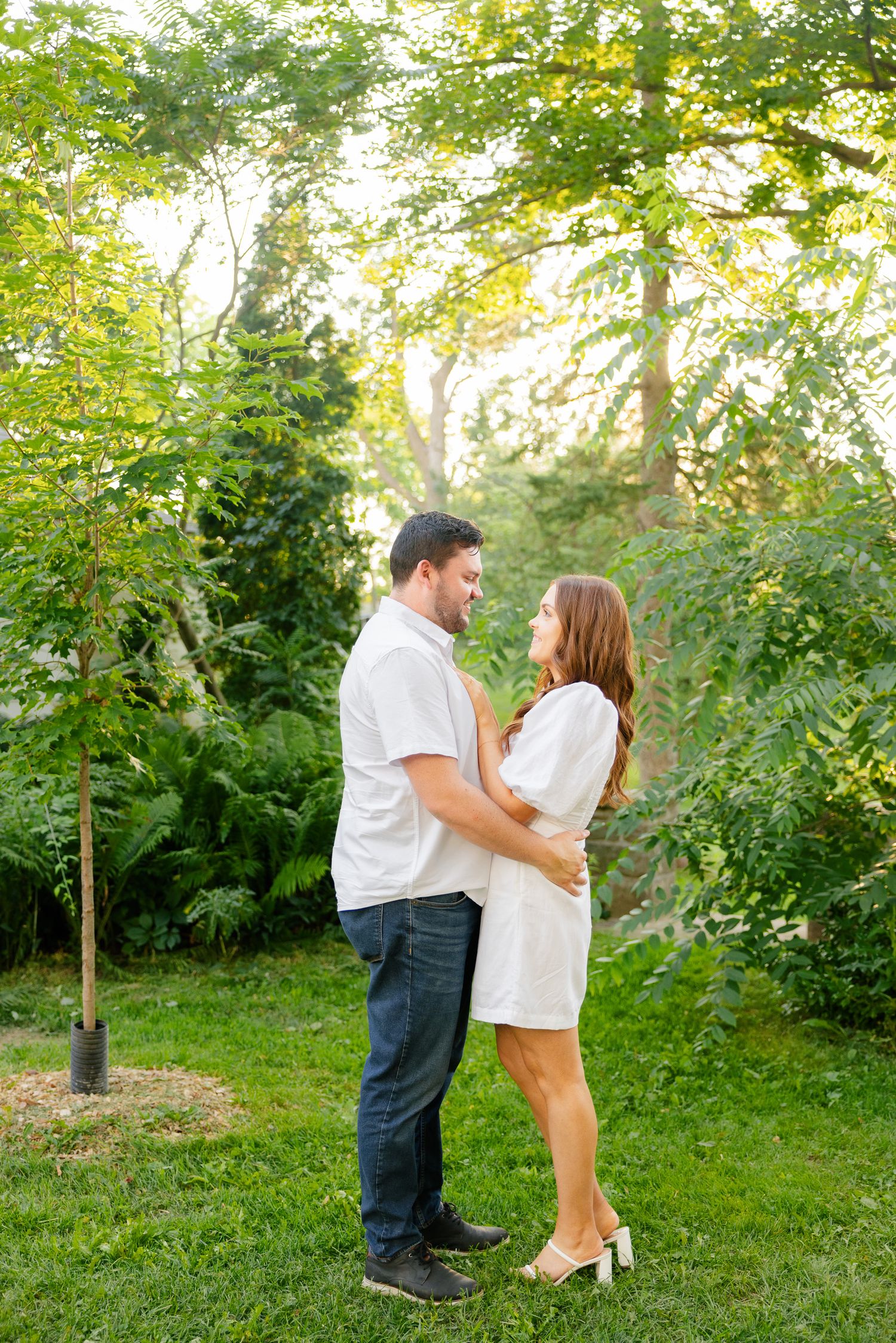 Couple in white clothing standing close together in a lush summer garden setting.