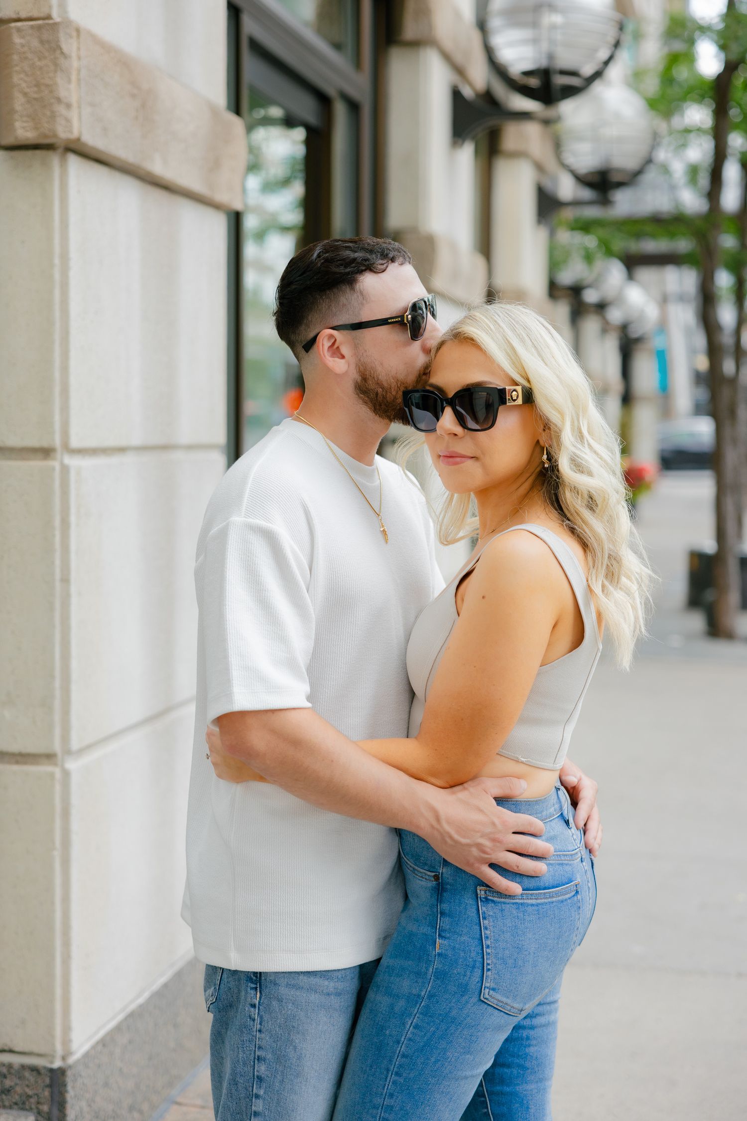 A stylish couple in sunglasses embracing on a city sidewalk.