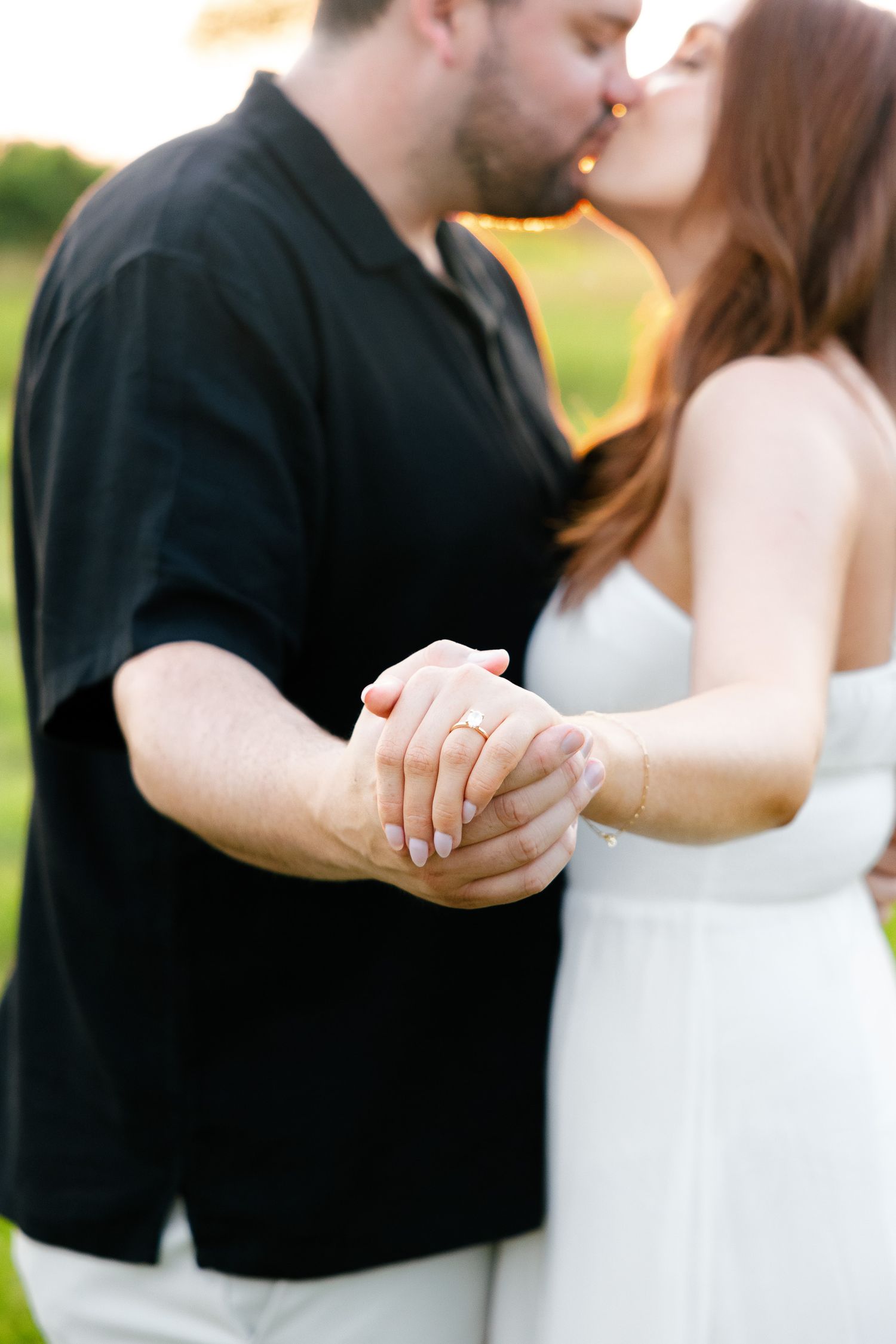 Close-up of couple holding hands while sharing kiss in sunset light.
