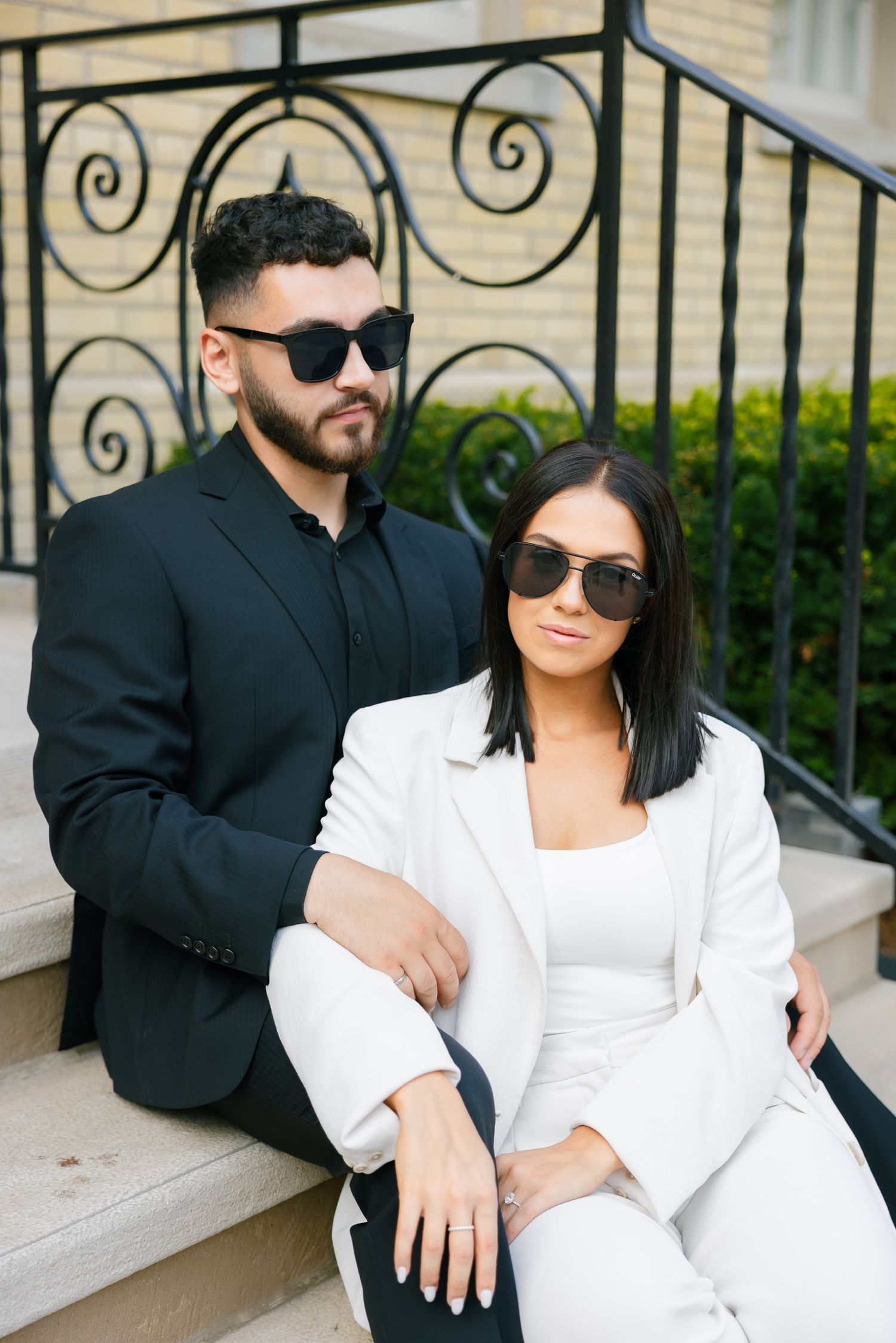 Fashionable duo in sunglasses and coordinated outfits pose on stone staircase.