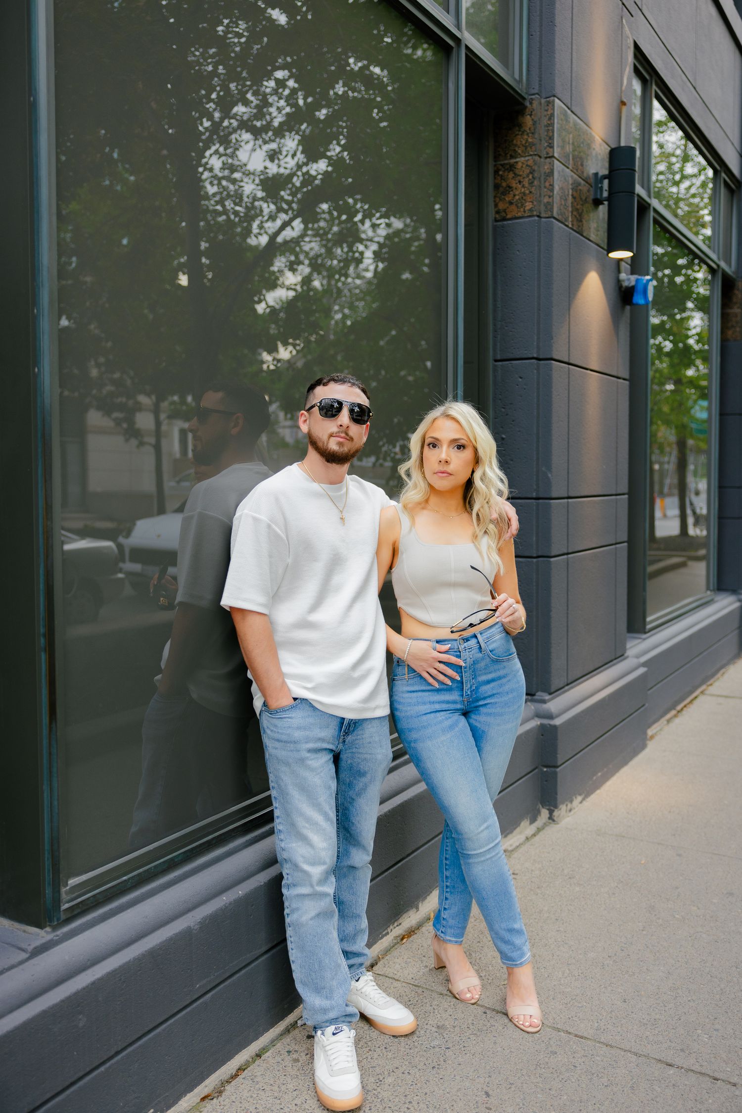 A fashionable couple in coordinated outfits pose against a commercial building exterior.