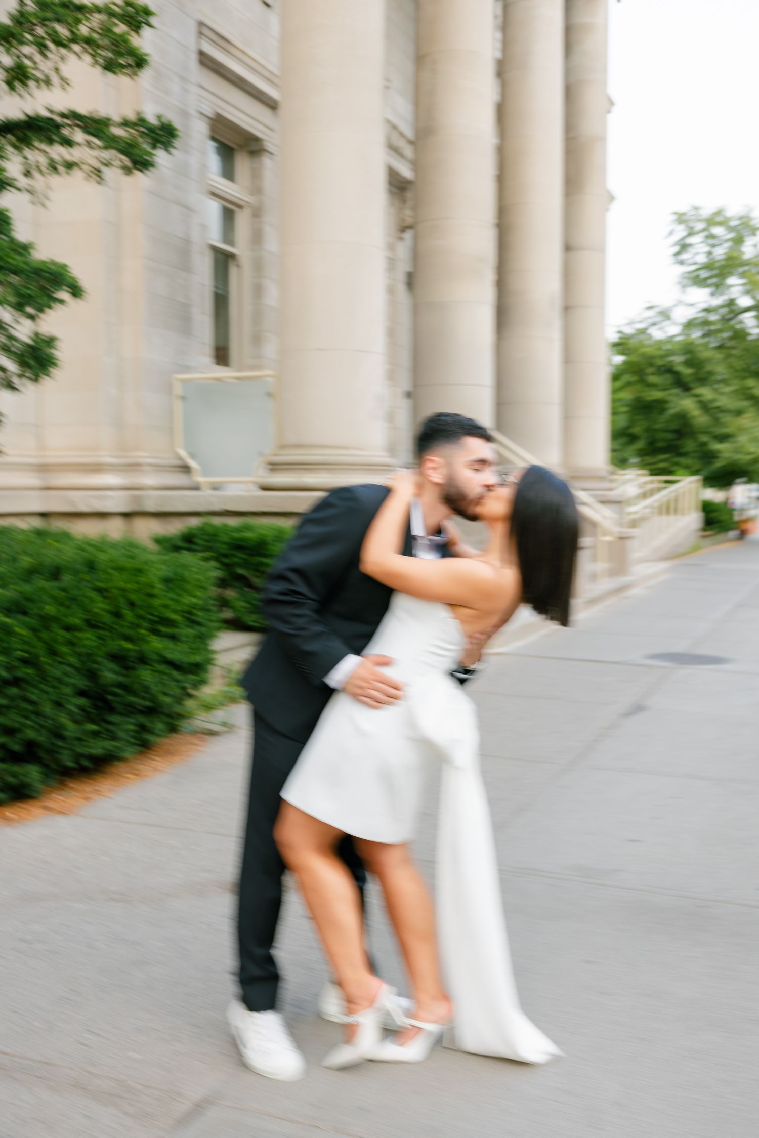 Blurred motion romantic moment between couple in formal wear near classical columns.